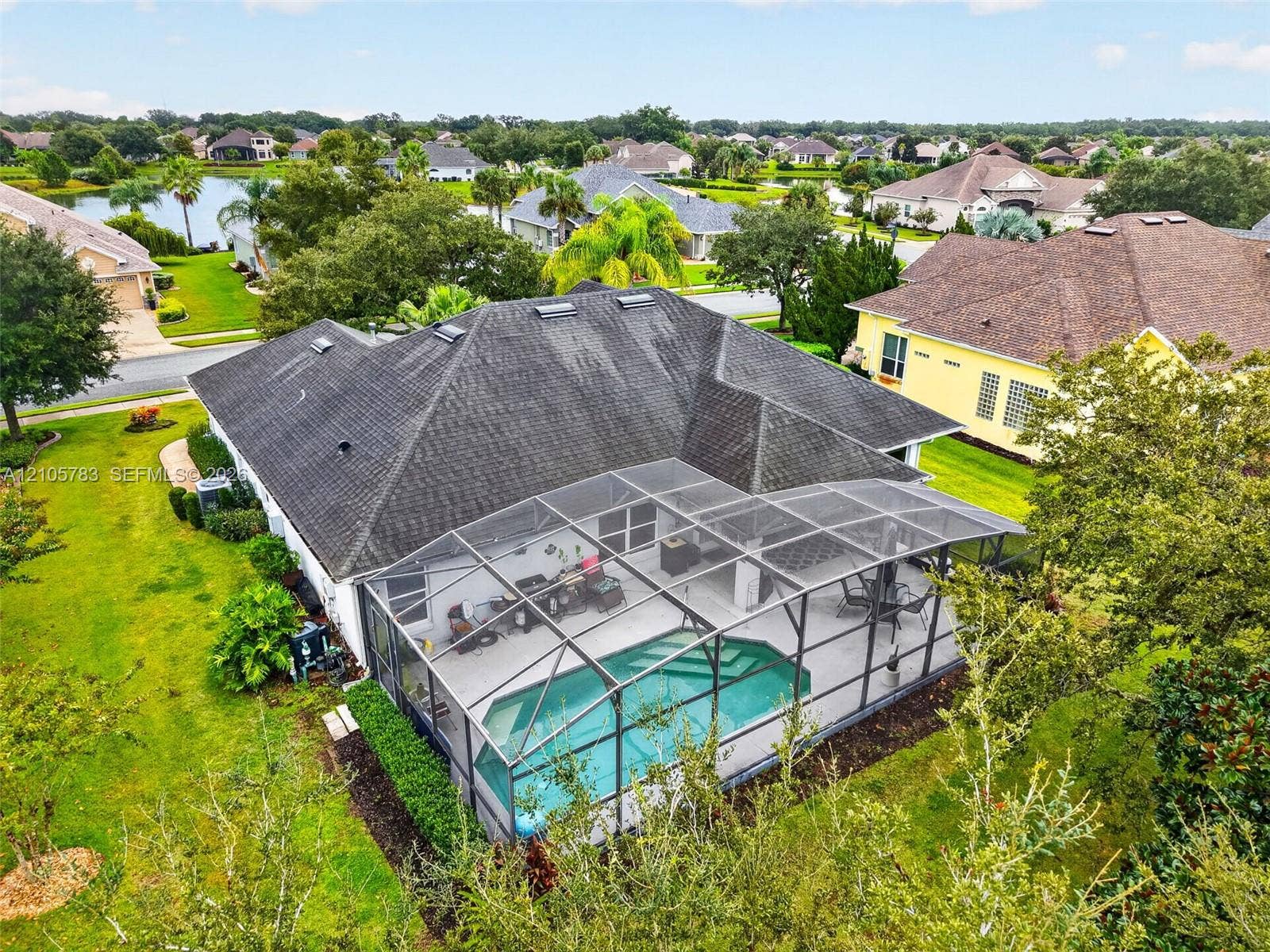 Single-story residence featuring a multi-hipped shingle roof with skylights, an expansive screened-in lanai, and an in-ground swimming pool