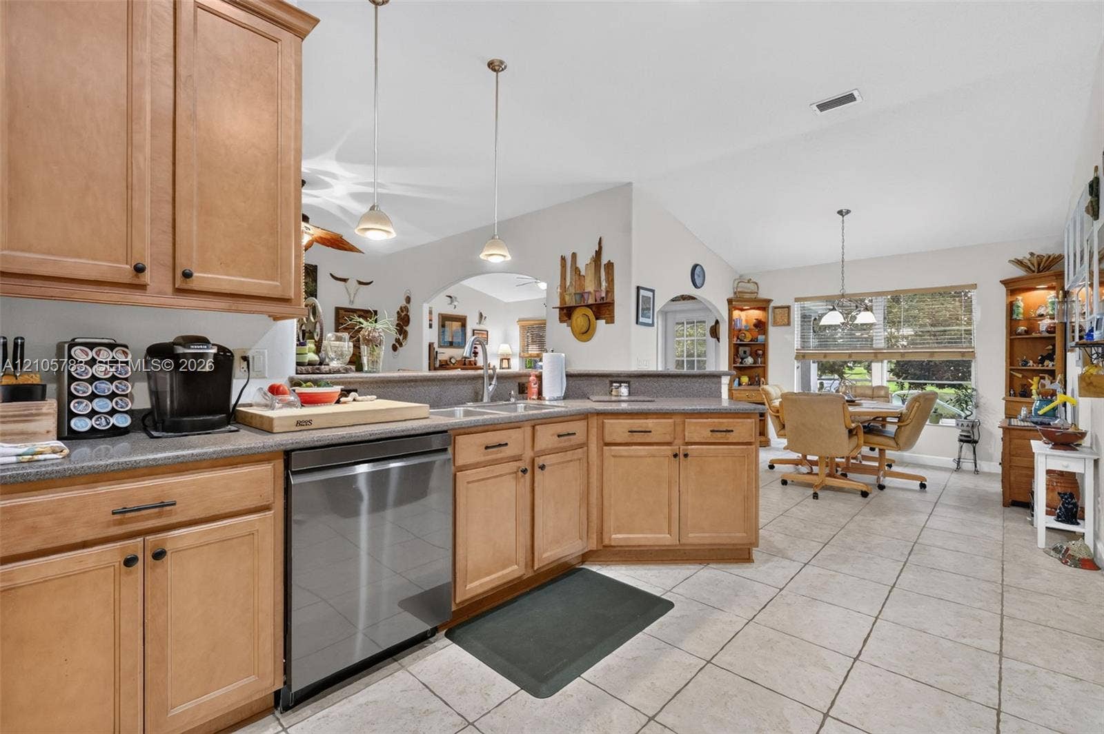 Kitchen featuring wood cabinetry, stone-finish countertops, stainless steel dishwasher, tile flooring, and pendant lighting