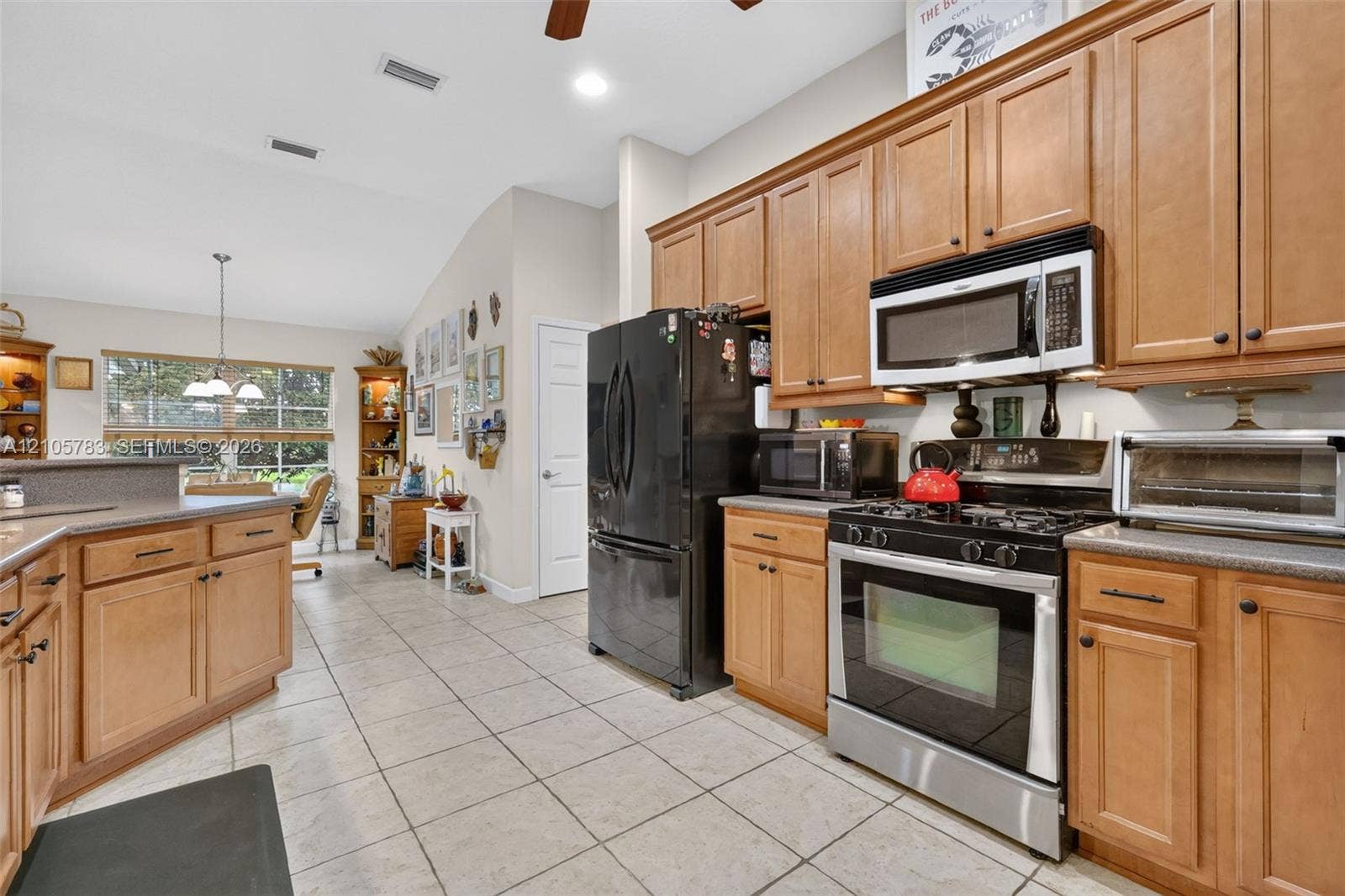 Kitchen featuring solid wood cabinetry, neutral stone-finish tile flooring, vaulted ceilings, integrated stainless steel appliances, and a breakfast bar