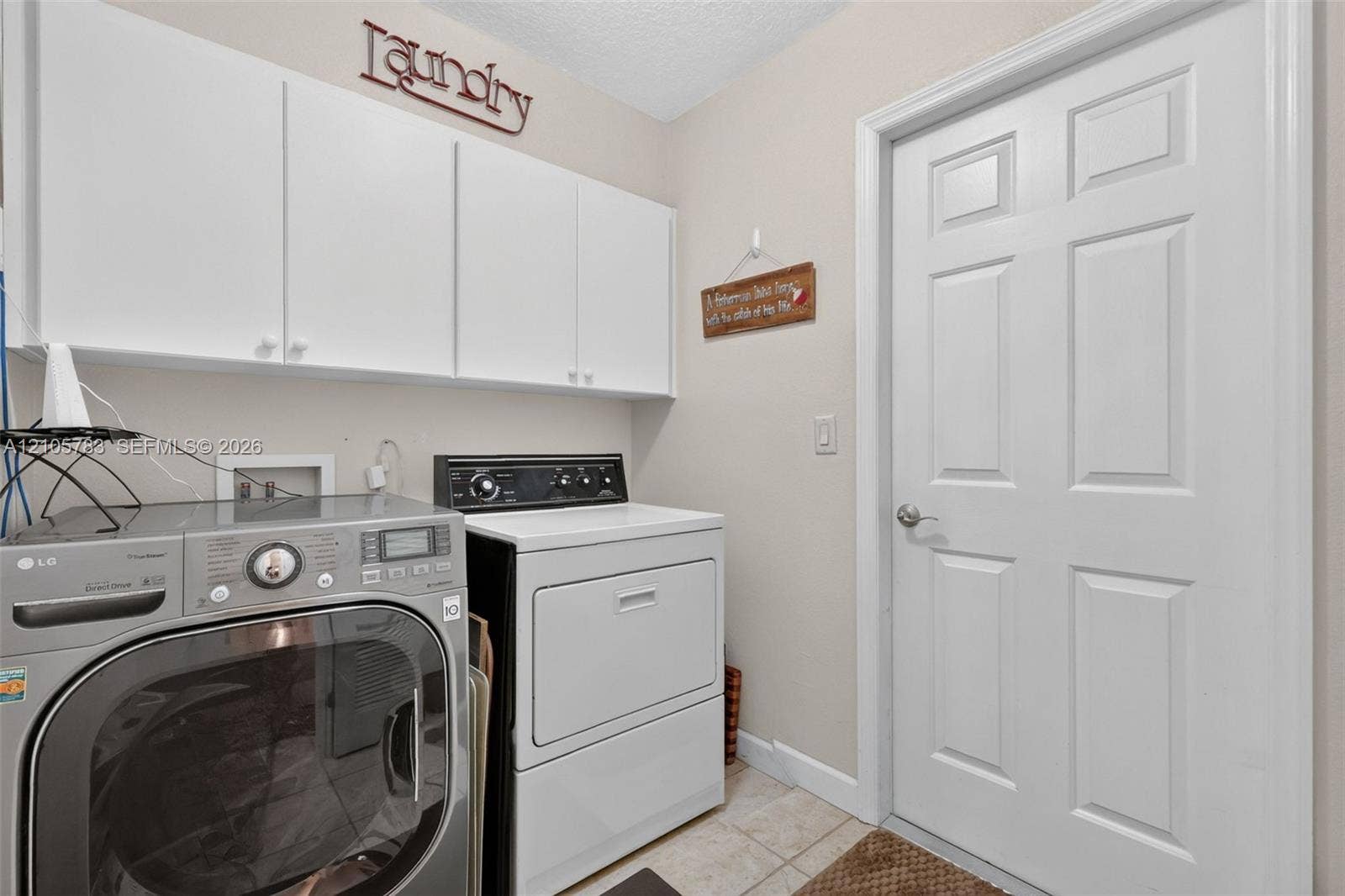 Laundry area featuring white cabinetry, neutral tile flooring, and a six-panel interior door