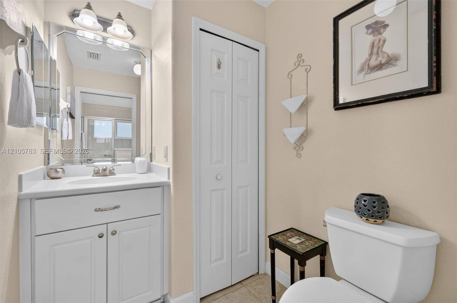White vanity featuring a solid surface countertop, undermount sink, and polished metal hardware, paired with a bi-fold closet door and wall-mounted light fixture