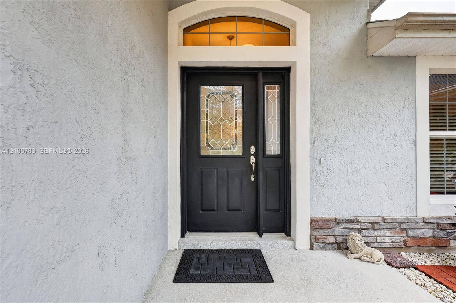 Entryway featuring a dark paneled door with leaded glass inlay, a matching sidelight, and an arched transom window, finished with stucco siding and stone veneer accents
