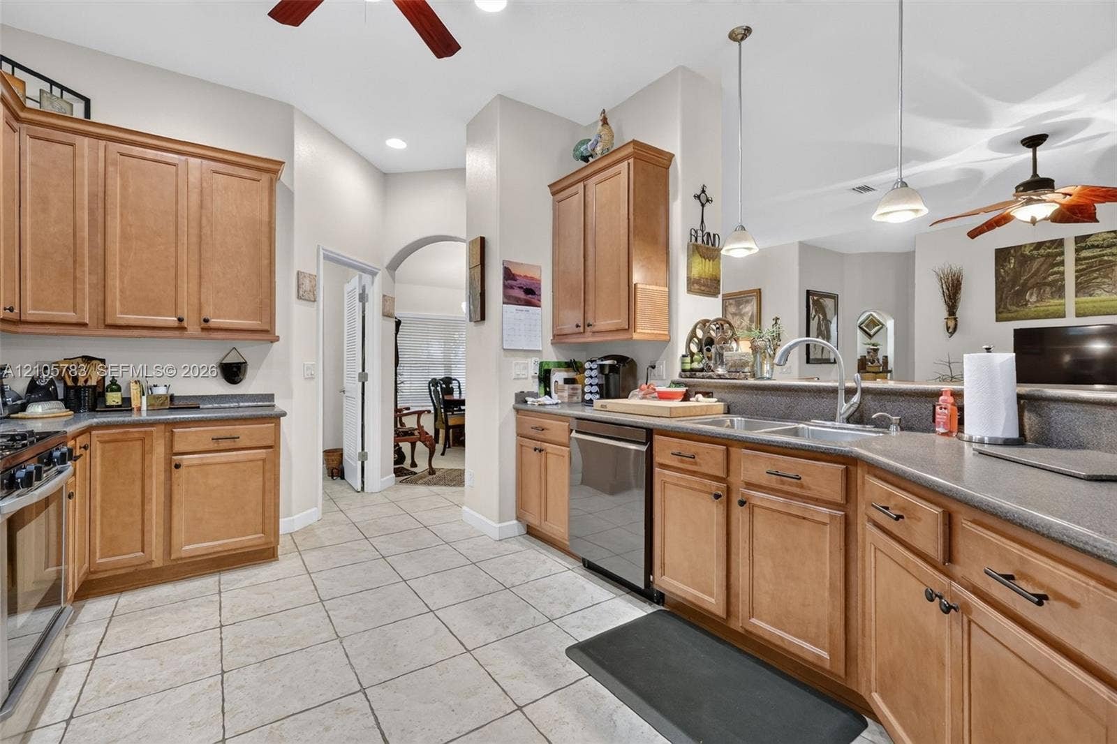Kitchen featuring medium-tone wood cabinetry, solid-surface countertops, tile flooring, dual-basin stainless steel sink with gooseneck faucet, and stainless steel dishwasher