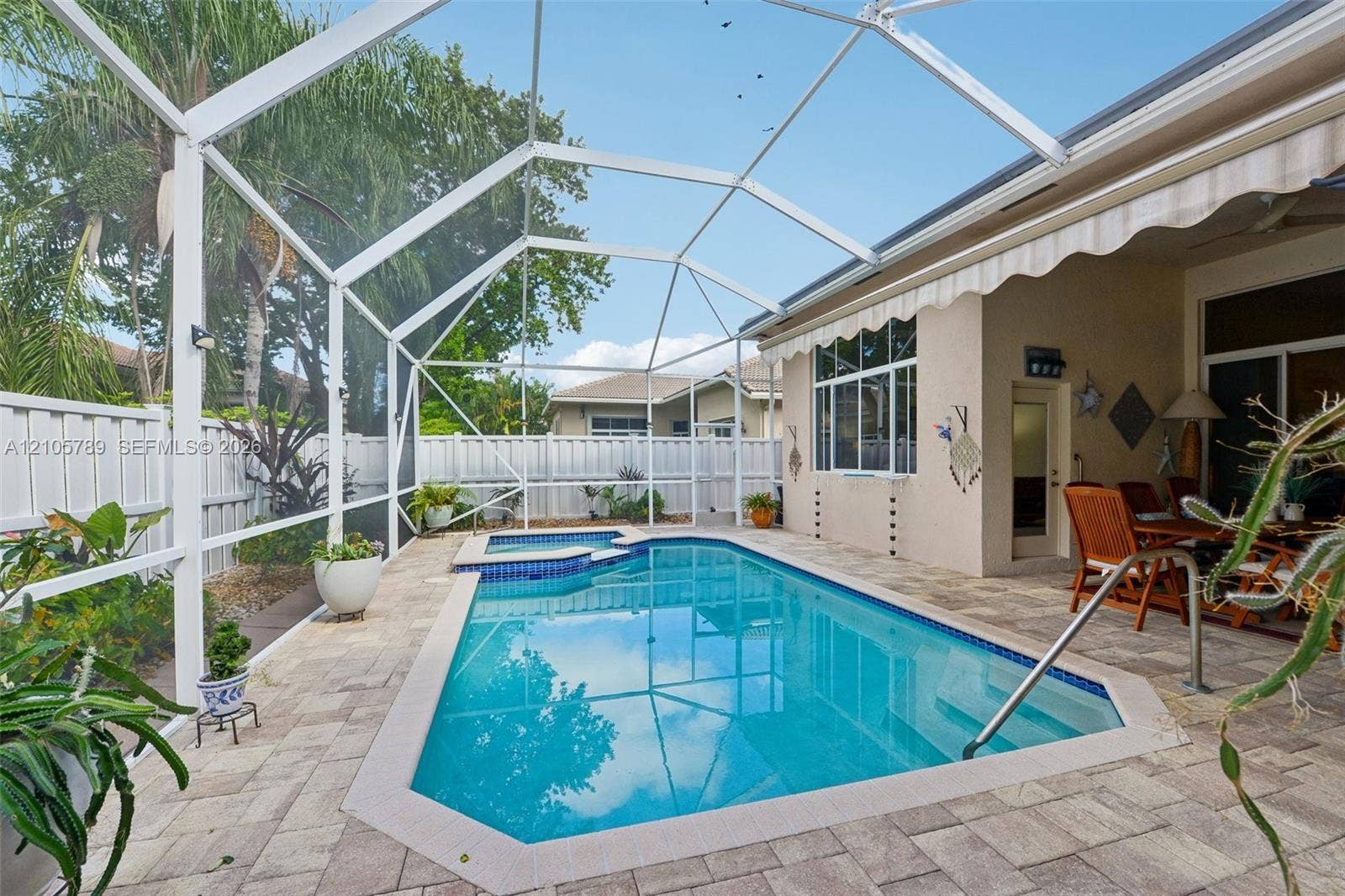 6353 SW 191st Avenue, Pembroke Pines, FL 33332 Screened-in patio featuring a swimming pool with an integrated spa, stone-paver decking, and white vinyl privacy fencing