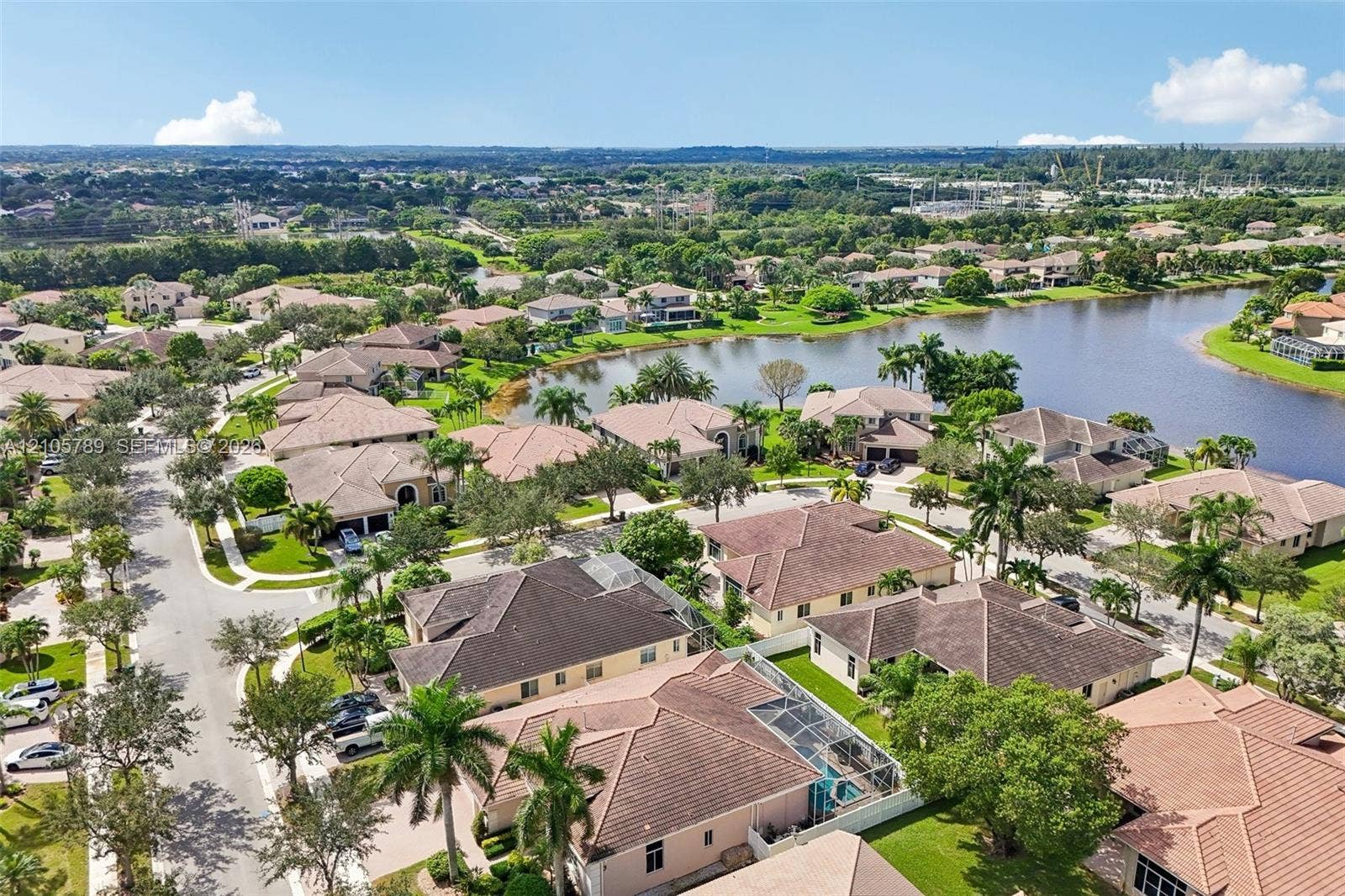 6353 SW 191st Avenue, Pembroke Pines, FL 33332 Aerial perspective of a residential community featuring expansive lake frontage, tile roofing, screened-in pool enclosures, and mature palm trees