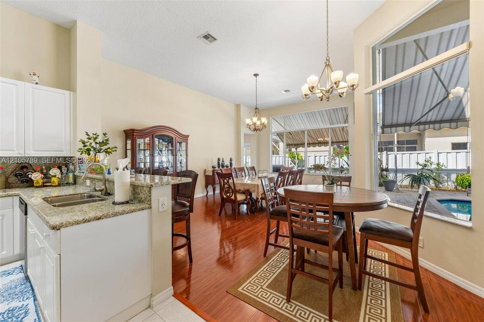 6353 SW 191st Avenue, Pembroke Pines, FL 33332 Kitchen featuring a stone countertop, white cabinetry, wood-finish flooring, dual decorative chandeliers, and high ceilings with large windows