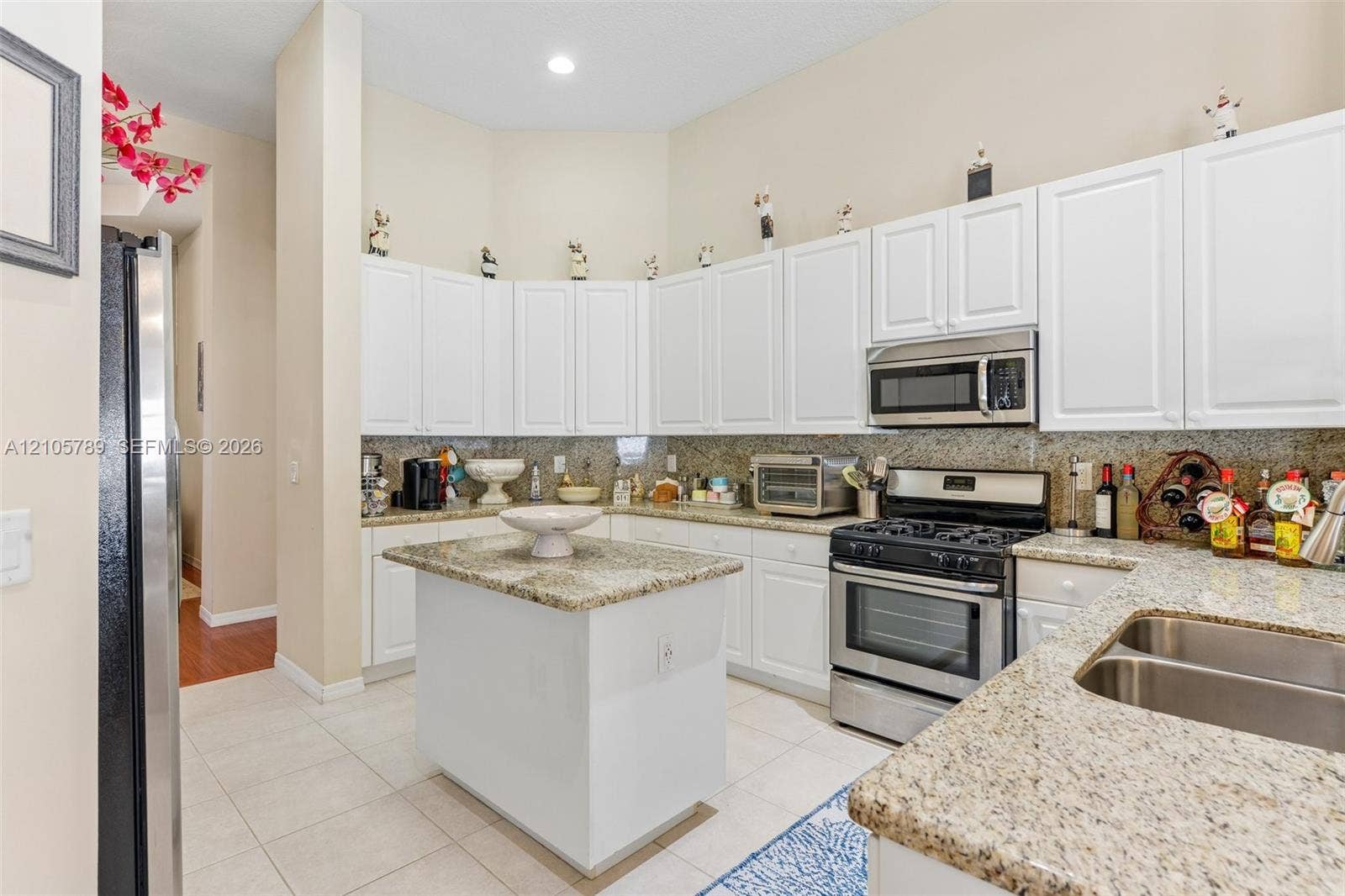 6353 SW 191st Avenue, Pembroke Pines, FL 33332 Kitchen featuring white shaker-style cabinetry, stone-finish countertops, central island, dual-basin stainless steel sink, and stainless steel appliances