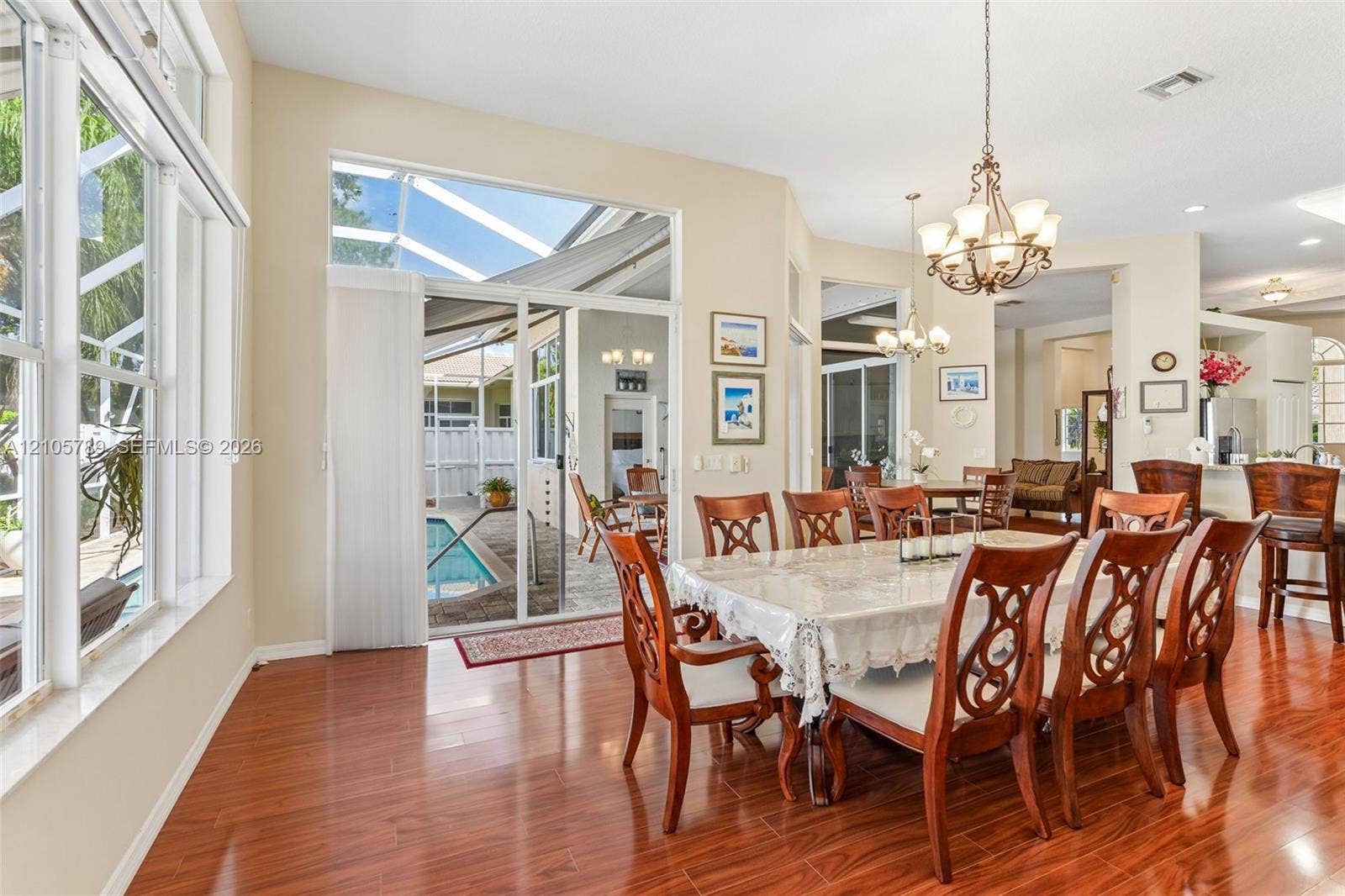 6353 SW 191st Avenue, Pembroke Pines, FL 33332 Dining area featuring wood-finish flooring, extensive windows, decorative chandeliers, and sliding glass doors leading to a screened-in lanai and pool enclosure