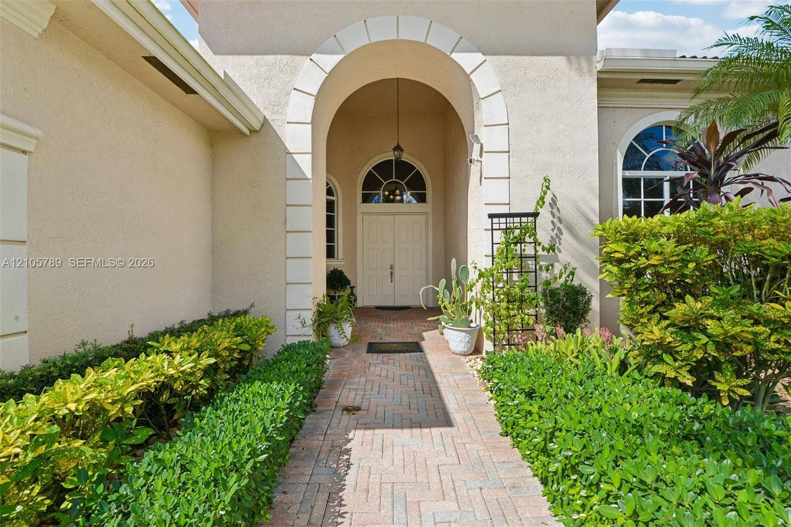 6353 SW 191st Avenue, Pembroke Pines, FL 33332 Stucco exterior entryway featuring a prominent arched portico with decorative quoins, double front doors with a semi-circular transom window, and a herringbone-patterned brick walkway