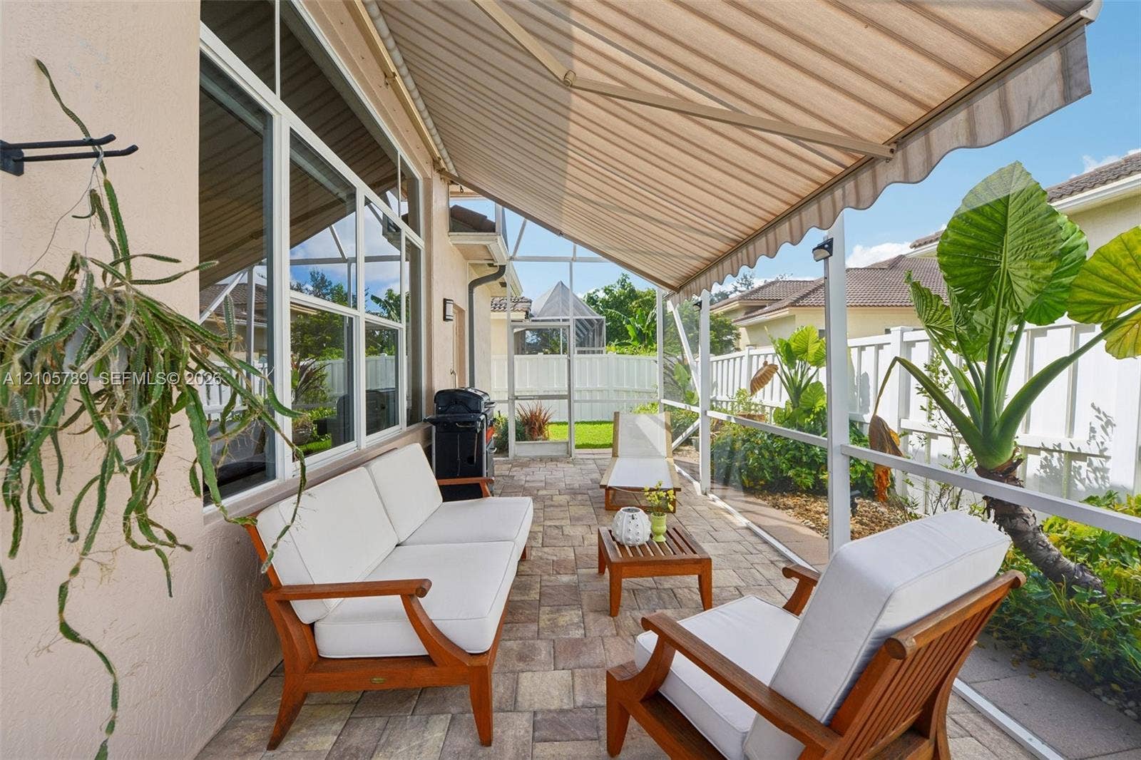 6353 SW 191st Avenue, Pembroke Pines, FL 33332 Screened-in patio featuring paver flooring, a retractable fabric awning, large multi-pane windows, and white vinyl perimeter fencing