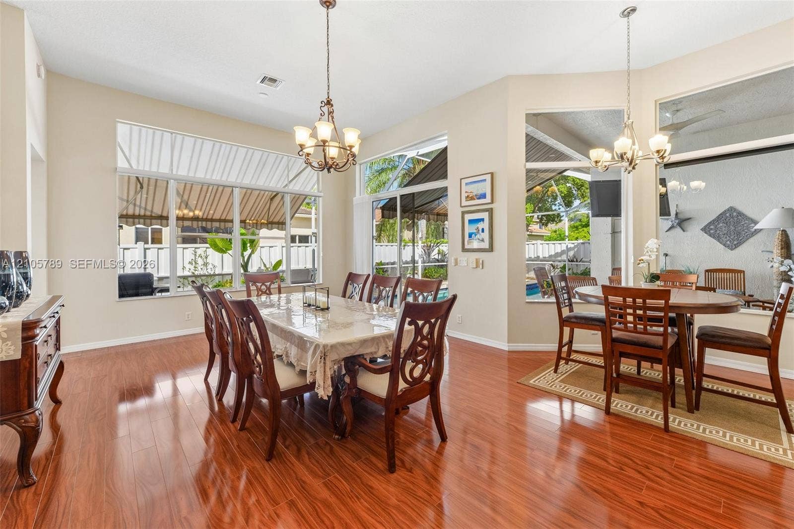 6353 SW 191st Avenue, Pembroke Pines, FL 33332 High-ceiling dining area featuring polished wood-finish flooring, extensive floor-to-ceiling windows, and dual multi-light pendant chandeliers