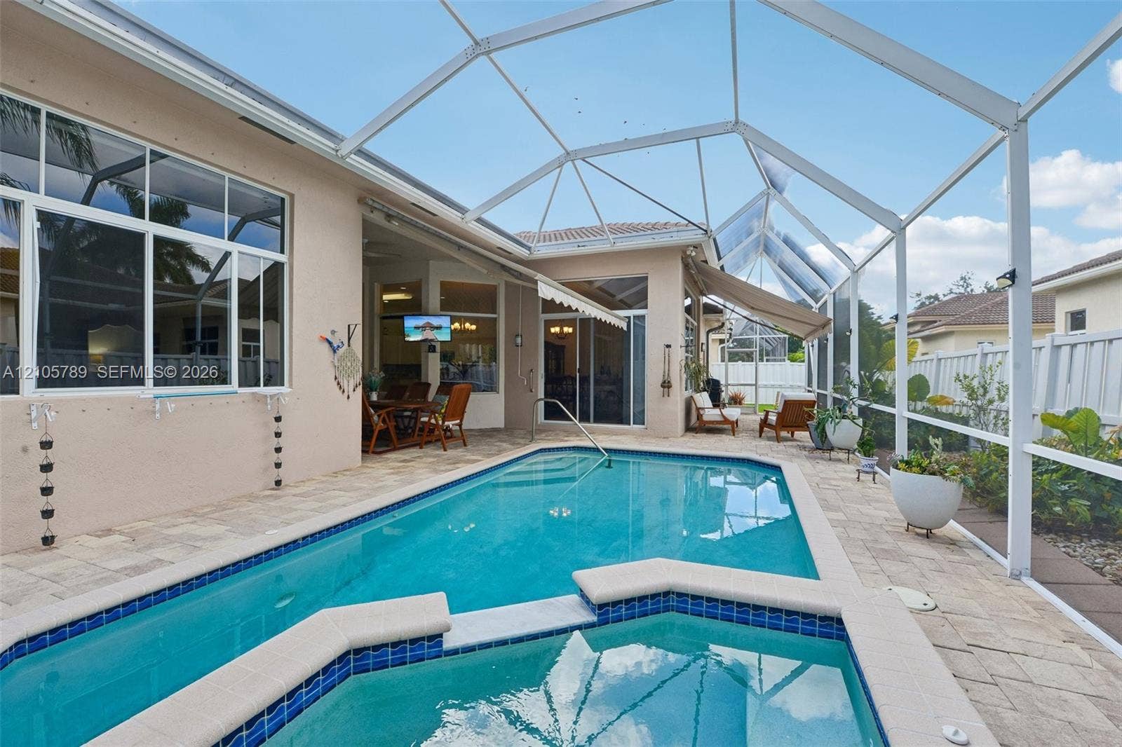 6353 SW 191st Avenue, Pembroke Pines, FL 33332 Screened outdoor enclosure featuring a swimming pool, integrated spa, stone-paver decking, and retractable fabric awnings