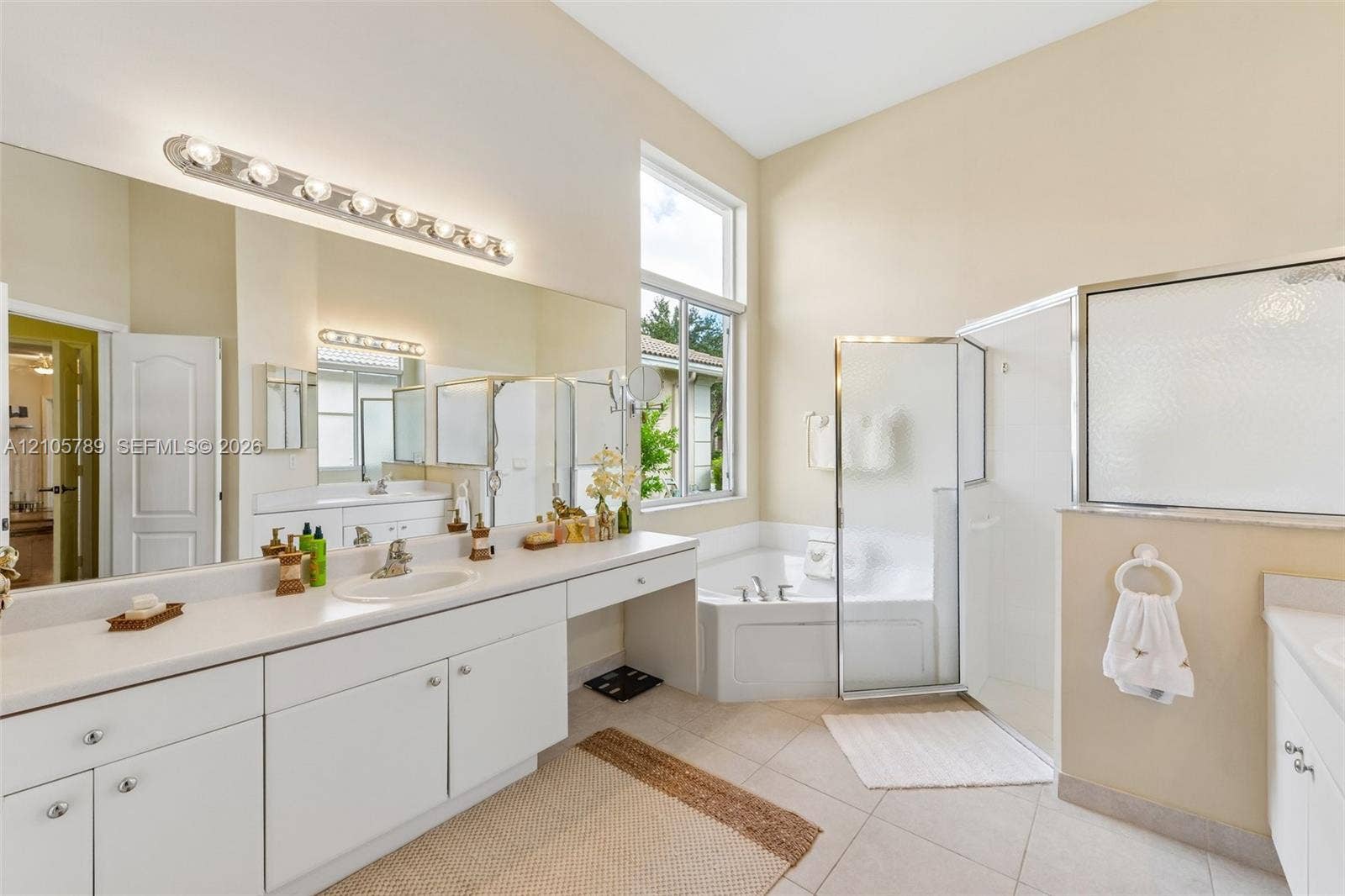 6353 SW 191st Avenue, Pembroke Pines, FL 33332 Bathroom featuring a dual-sink vanity with white cabinetry and solid-surface countertops, a corner soaking tub, and a glass-enclosed shower