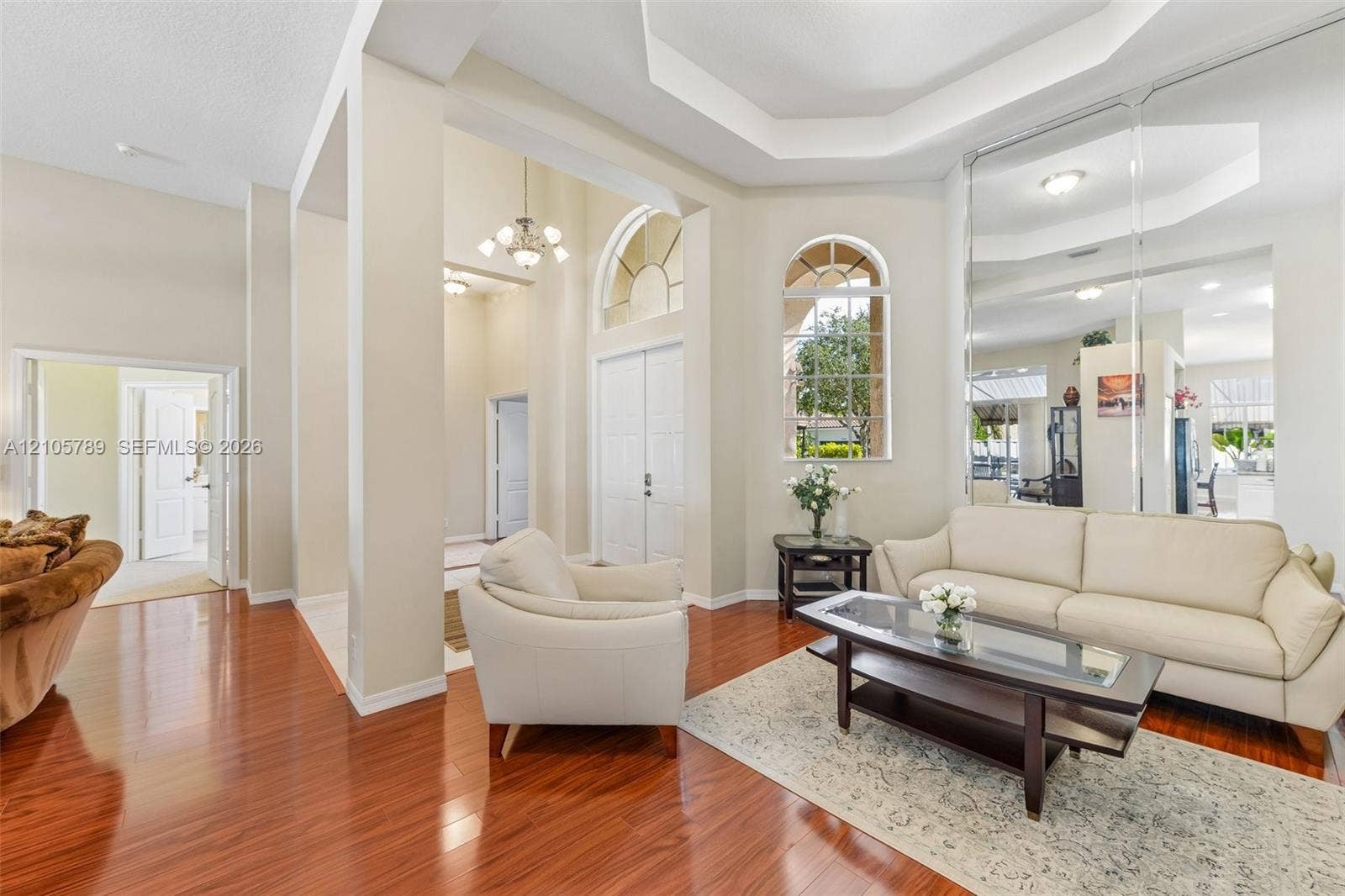 6353 SW 191st Avenue, Pembroke Pines, FL 33332 Living area featuring high ceilings with crown molding, wood-finish flooring, full-wall mirrors, arched windows, and double-entry doors