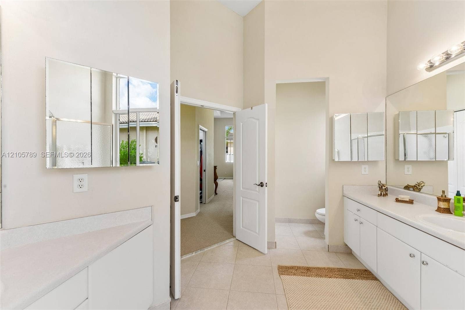 6353 SW 191st Avenue, Pembroke Pines, FL 33332 Bathroom featuring high ceilings, white cabinetry, dual mirrored medicine cabinets, and tile flooring