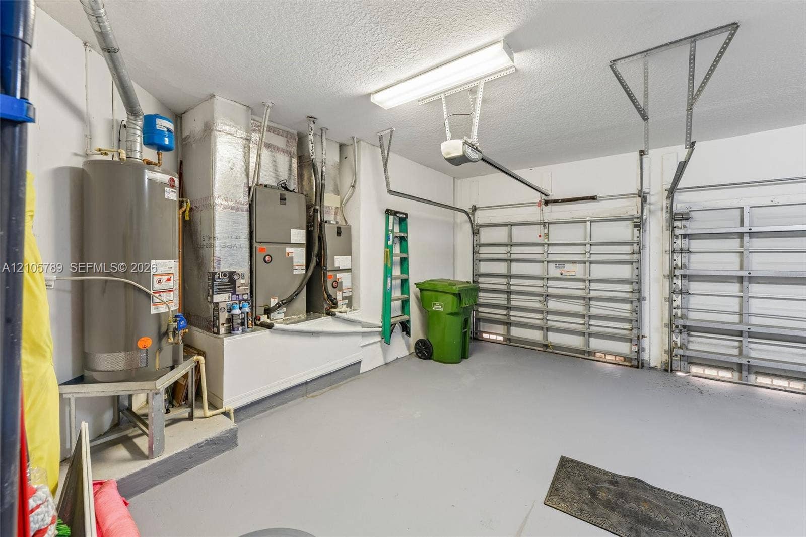 6353 SW 191st Avenue, Pembroke Pines, FL 33332 Two-car garage featuring dual overhead metal doors, painted concrete flooring, and built-in mechanical systems including a water heater and HVAC unit