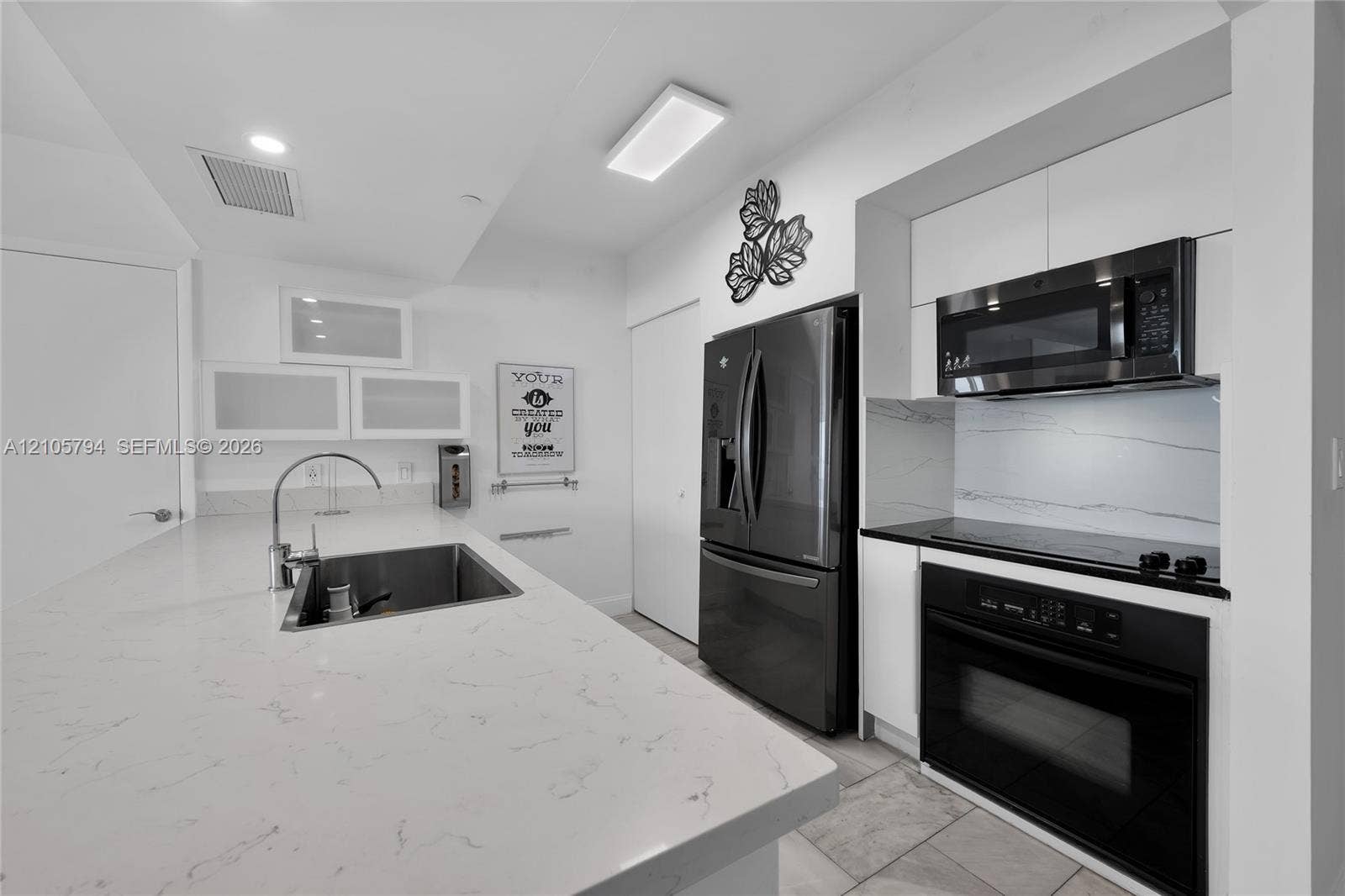 1830 S Ocean Drive, #4210, Hallandale Beach, Hallandale Beach, FL 33009 Kitchen featuring a central island with a stone-finish countertop and undermount sink, white cabinetry with frosted glass accents, stone-finish backsplash, built-in stainless steel microwave and oven, and dark-toned full-size refrigerator