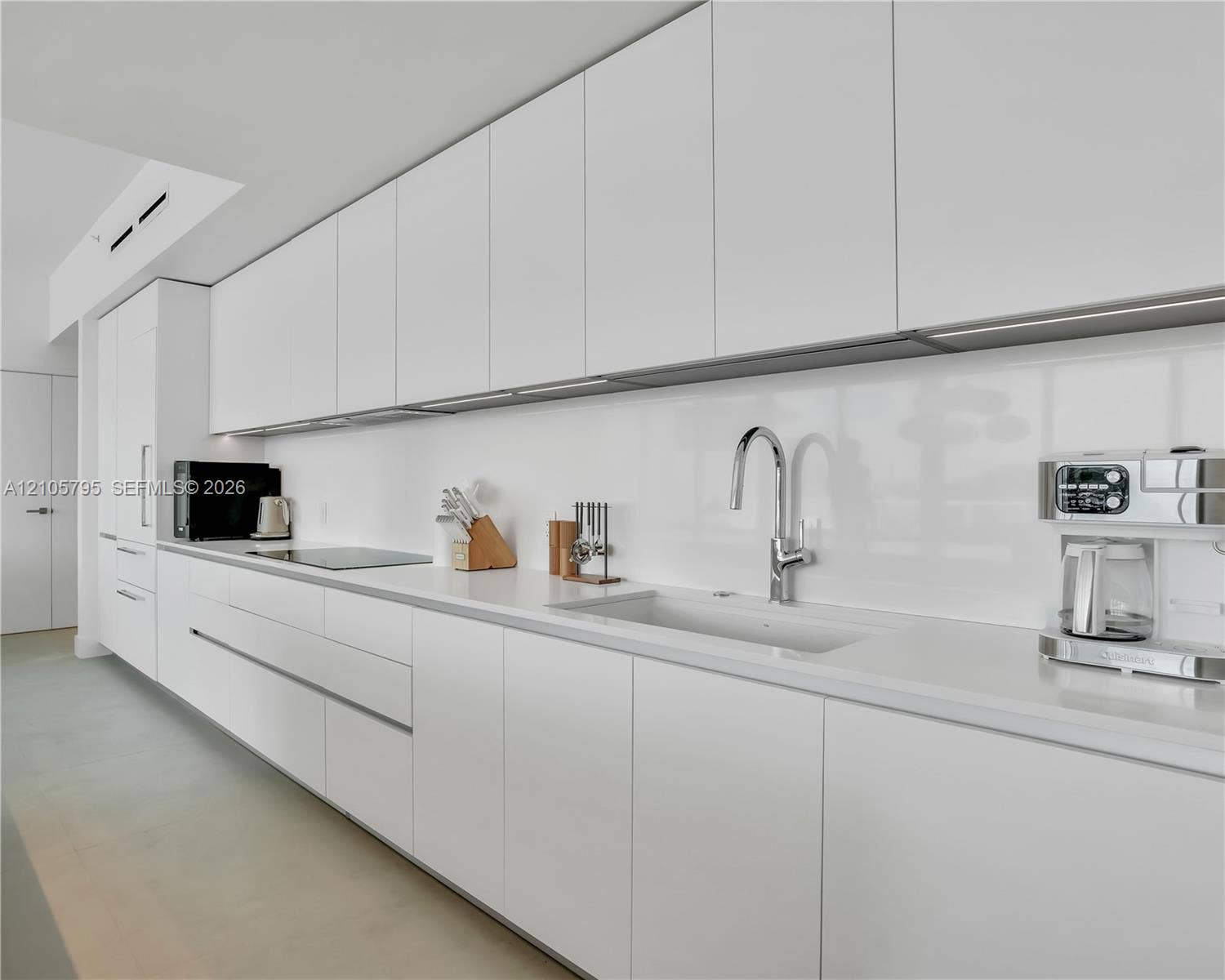 407 N Riverside Drive, #202, Pompano Beach, Pompano Beach, FL 33062 Minimalist kitchen featuring flat-panel cabinetry, solid-surface countertops, a seamless backsplash, an integrated induction cooktop, and a chrome gooseneck faucet
