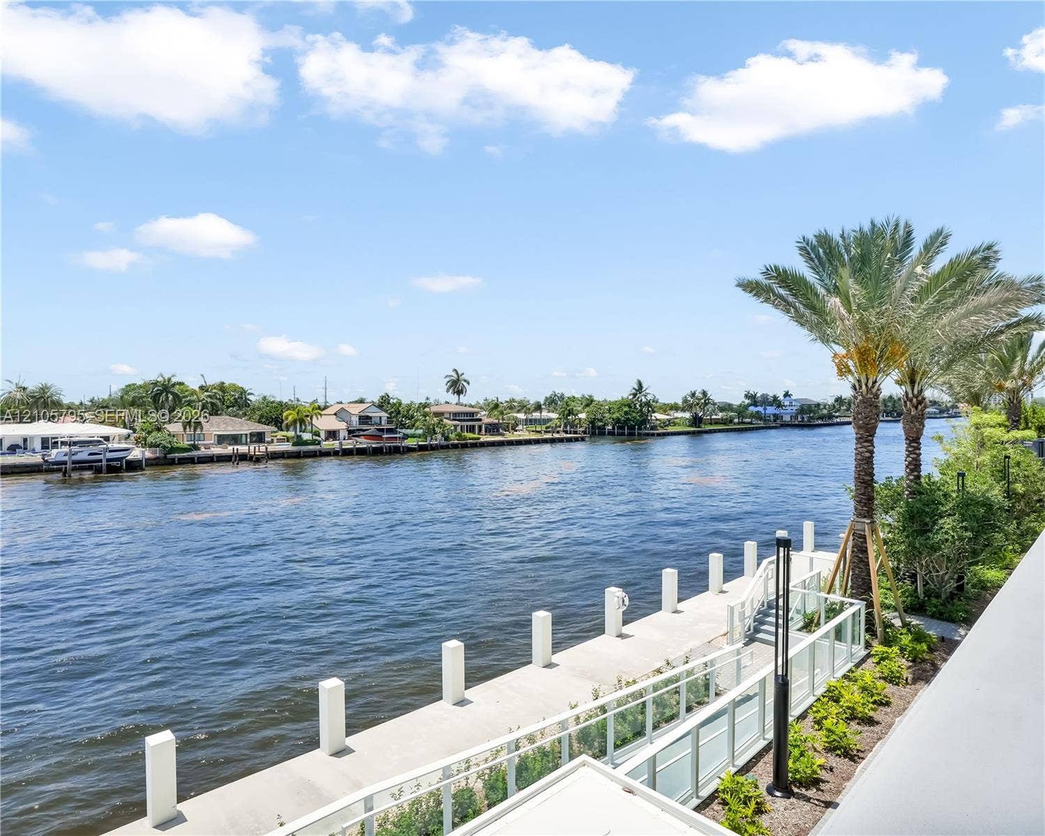 407 N Riverside Drive, #202, Pompano Beach, Pompano Beach, FL 33062 Waterfront property featuring a concrete seawall, glass panel railing, paved walkway, and mature palm trees