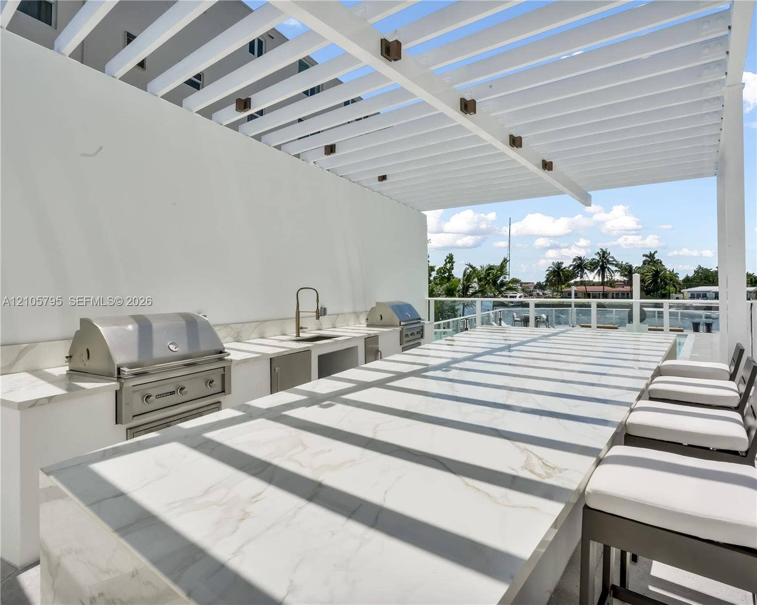 407 N Riverside Drive, #202, Pompano Beach, Pompano Beach, FL 33062 Outdoor kitchen featuring a stone-surface island, integrated stainless steel gas grill, undermount sink with a gooseneck faucet, and an overhead pergola