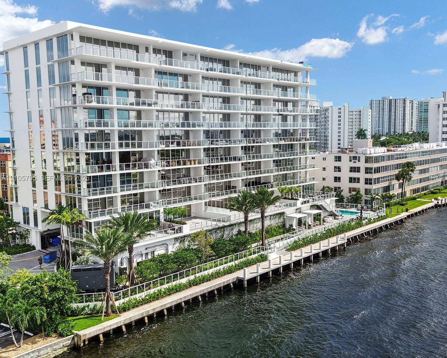 407 N Riverside Drive, #202, Pompano Beach, Pompano Beach, FL 33062 Modern mid-rise building featuring floor-to-ceiling glass windows, wraparound glass-panel balconies, a waterfront bulkhead, and a paved canal-side walkway
