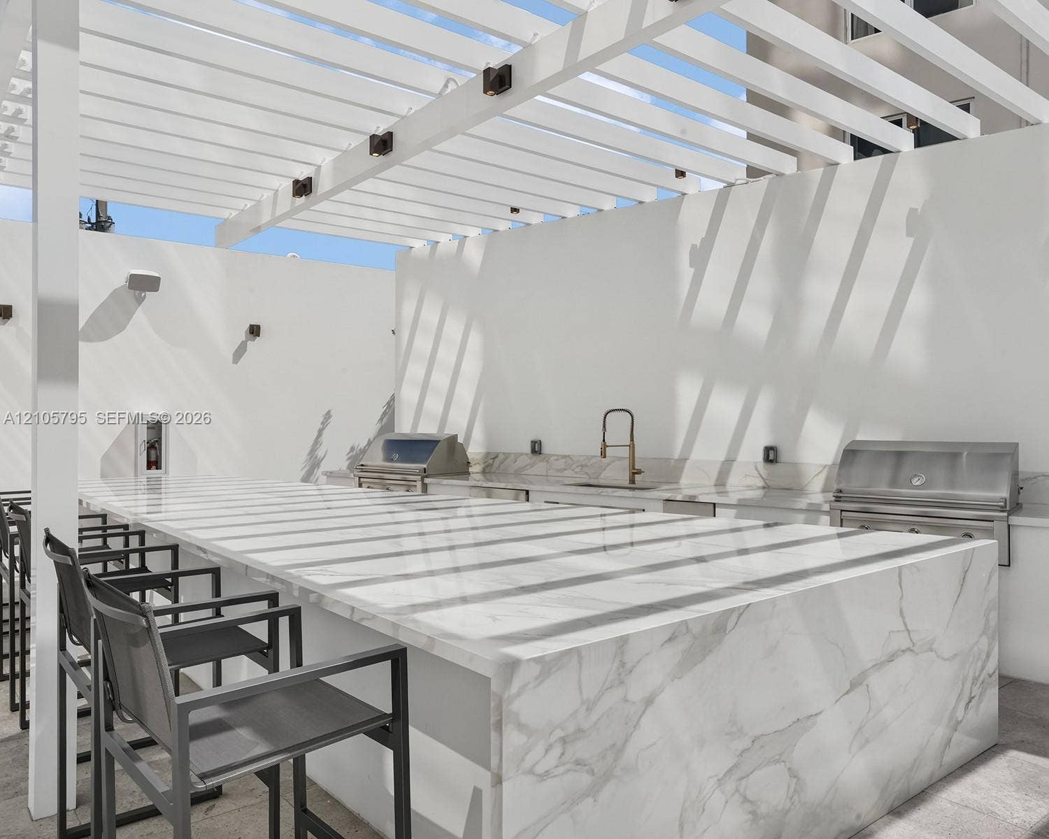 407 N Riverside Drive, #202, Pompano Beach, Pompano Beach, FL 33062 Outdoor kitchen featuring a large waterfall-edge countertop, stainless steel grill, undermount sink with a gooseneck faucet, and a white overhead pergola