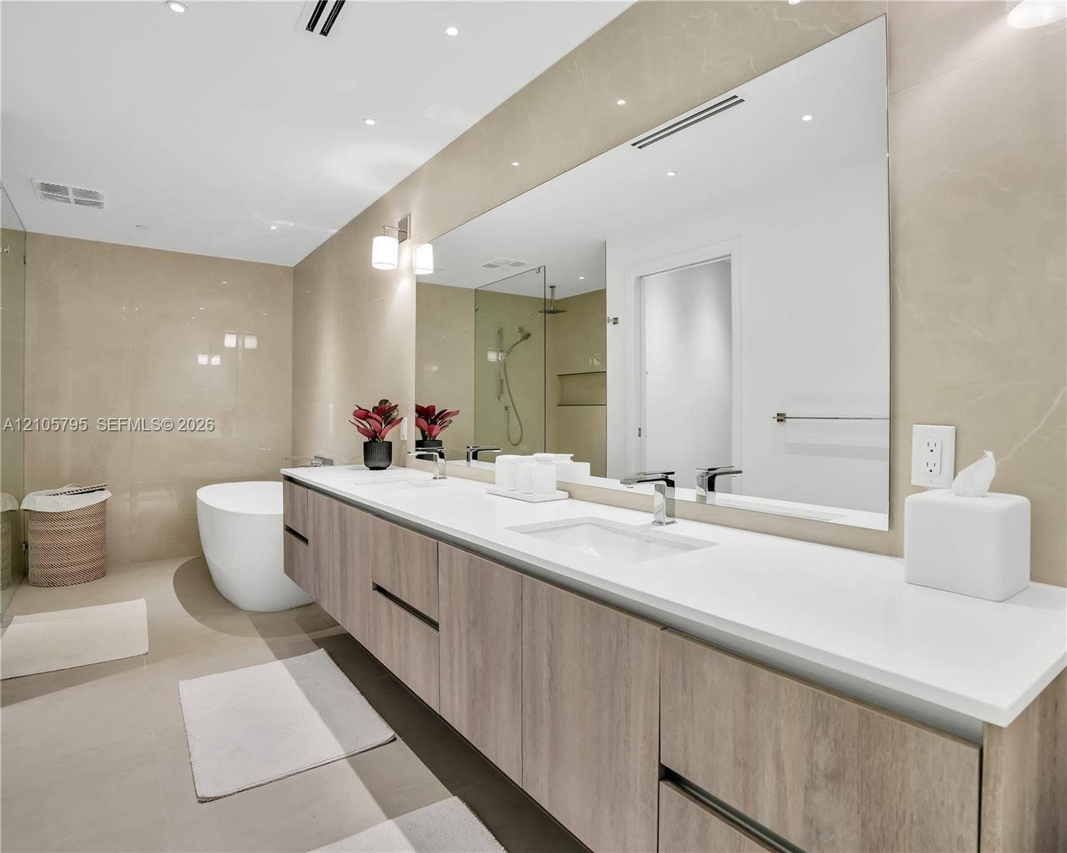407 N Riverside Drive, #202, Pompano Beach, Pompano Beach, FL 33062 Floating dual-sink vanity featuring wood-finish cabinetry, solid surface countertops, polished chrome fixtures, and a large frameless wall-to-wall mirror, complemented by a freestanding soaking tub and full-height tiled wall surround
