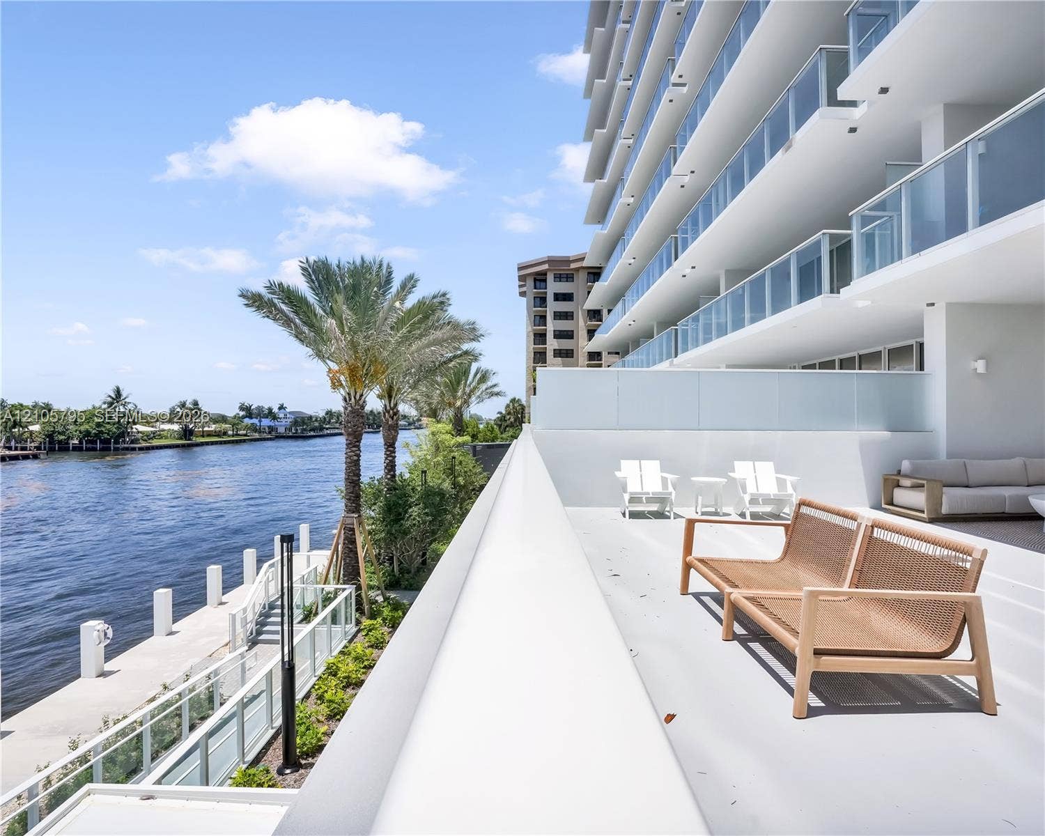 407 N Riverside Drive, #202, Pompano Beach, Pompano Beach, FL 33062 Expansive private balcony featuring glass panel railings, concrete flooring, and direct water frontage overlooking the waterway, complemented by a stone-paved bulkhead and integrated lighting