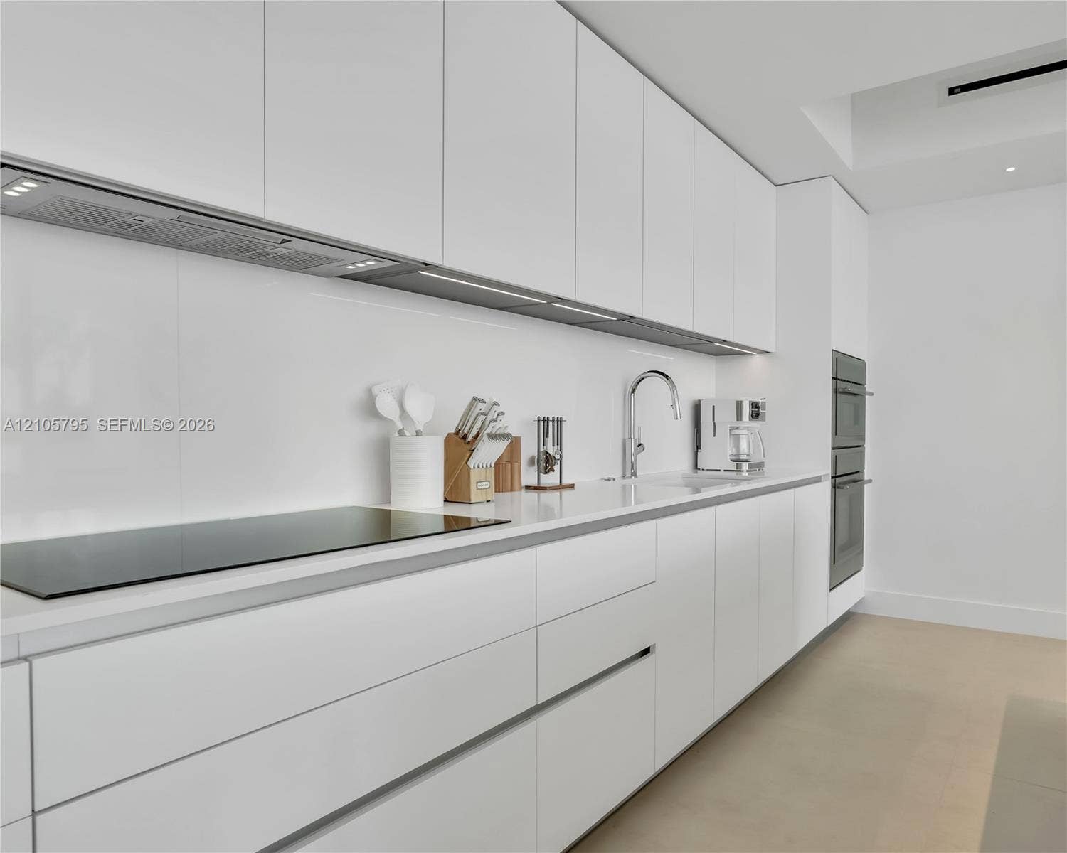 407 N Riverside Drive, #202, Pompano Beach, Pompano Beach, FL 33062 Minimalist kitchen featuring matte white flat-panel cabinetry, smooth white countertops, integrated cooktop, chrome gooseneck faucet, and stainless steel built-in wall oven