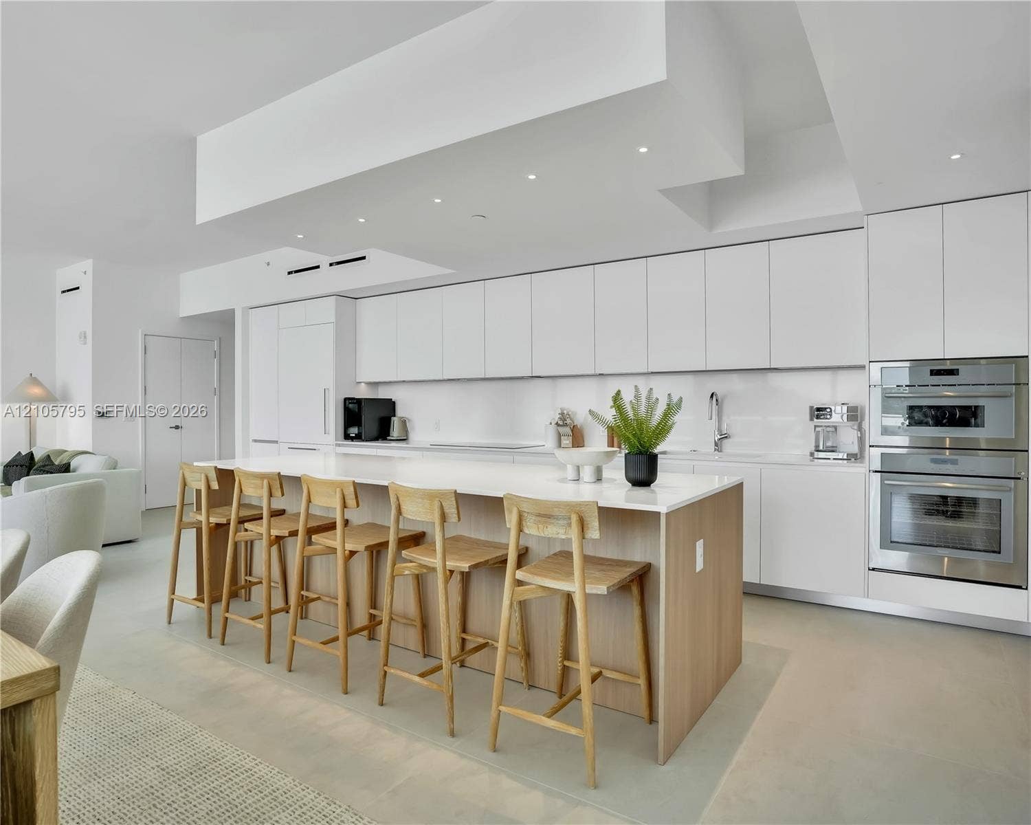 407 N Riverside Drive, #202, Pompano Beach, Pompano Beach, FL 33062 Modern kitchen featuring seamless flat-panel white cabinetry, a waterfall-edge central island with wood-finish base, integrated stainless steel double wall ovens, recessed ceiling lighting, and smooth-finish flooring