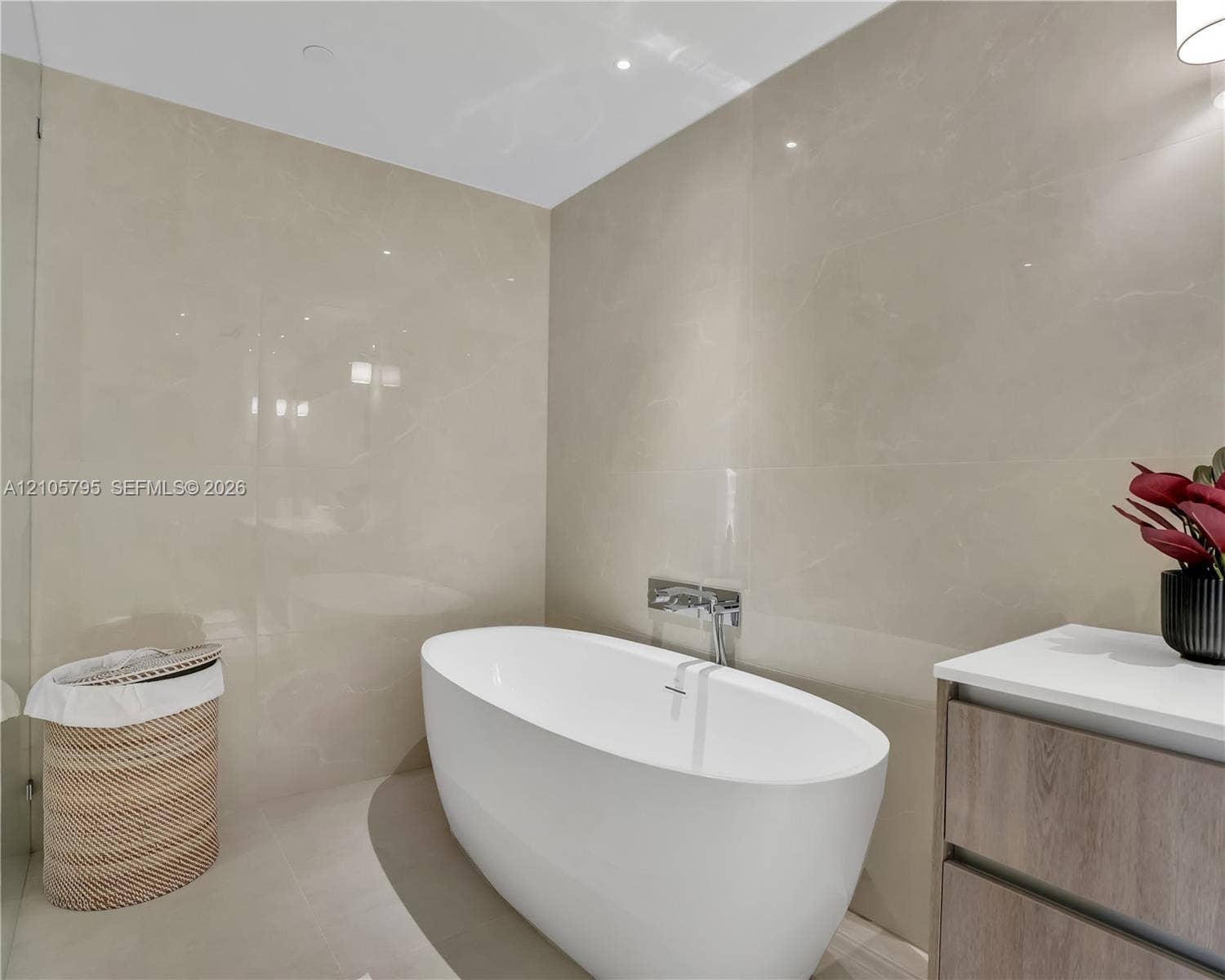 407 N Riverside Drive, #202, Pompano Beach, Pompano Beach, FL 33062 Freestanding white soaking tub with wall-mounted polished chrome faucet, floor-to-ceiling large-format tile wall cladding, and wood-finish vanity cabinet with a white countertop