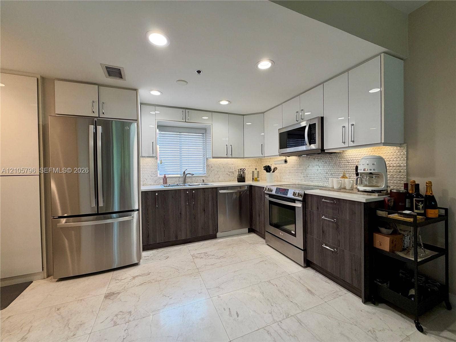 1611 SW 2nd Court, #A111, Miami, FL 33129 Kitchen featuring two-tone cabinetry with white upper and wood-finish lower cupboards, stone-patterned floor tiling, stainless steel appliances, and a mosaic tile backsplash