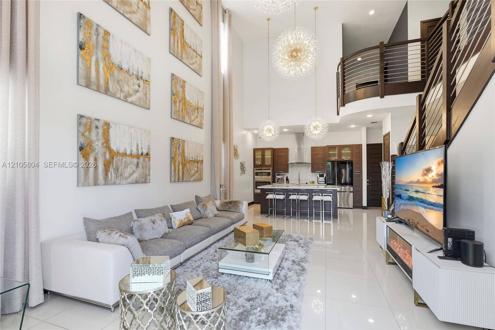 15932 SW 136th Way, Miami, FL 33196 Double-height ceilings, porcelain tile flooring, kitchen featuring custom wood cabinetry and stainless steel appliances, tiered pendant lighting, and metal railed mezzanine overlook