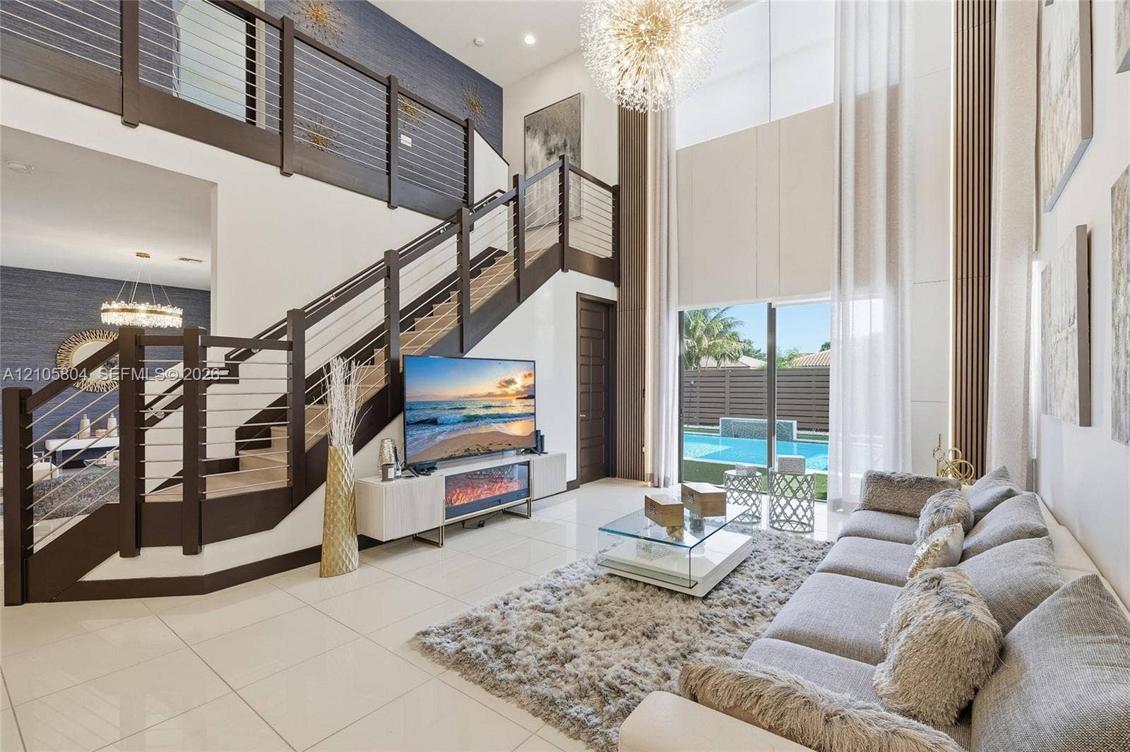 15932 SW 136th Way, Miami, FL 33196 Double-height living area featuring large-format tile flooring, a custom staircase with dark wood-finish treads and a horizontal cable railing system, a recessed electric fireplace, and floor-to-ceiling windows
