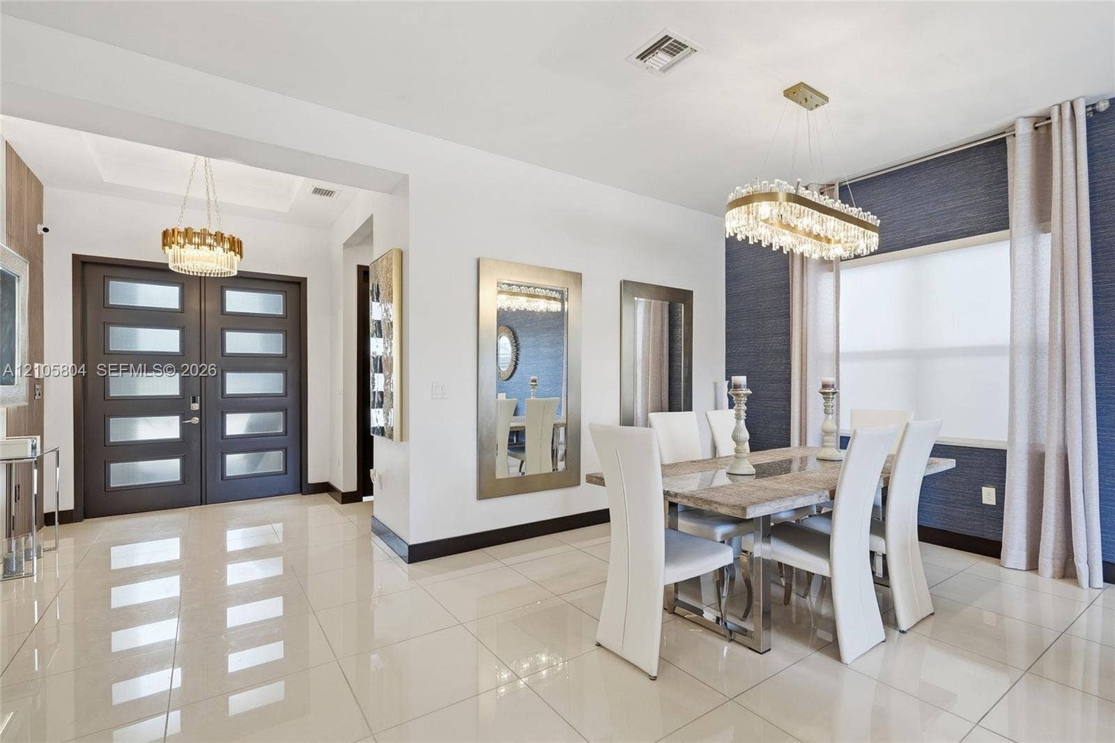 15932 SW 136th Way, Miami, FL 33196 Dining area featuring large-format tile flooring, textured wall covering, custom linear crystal chandelier, and double front entry doors with frosted glass panels