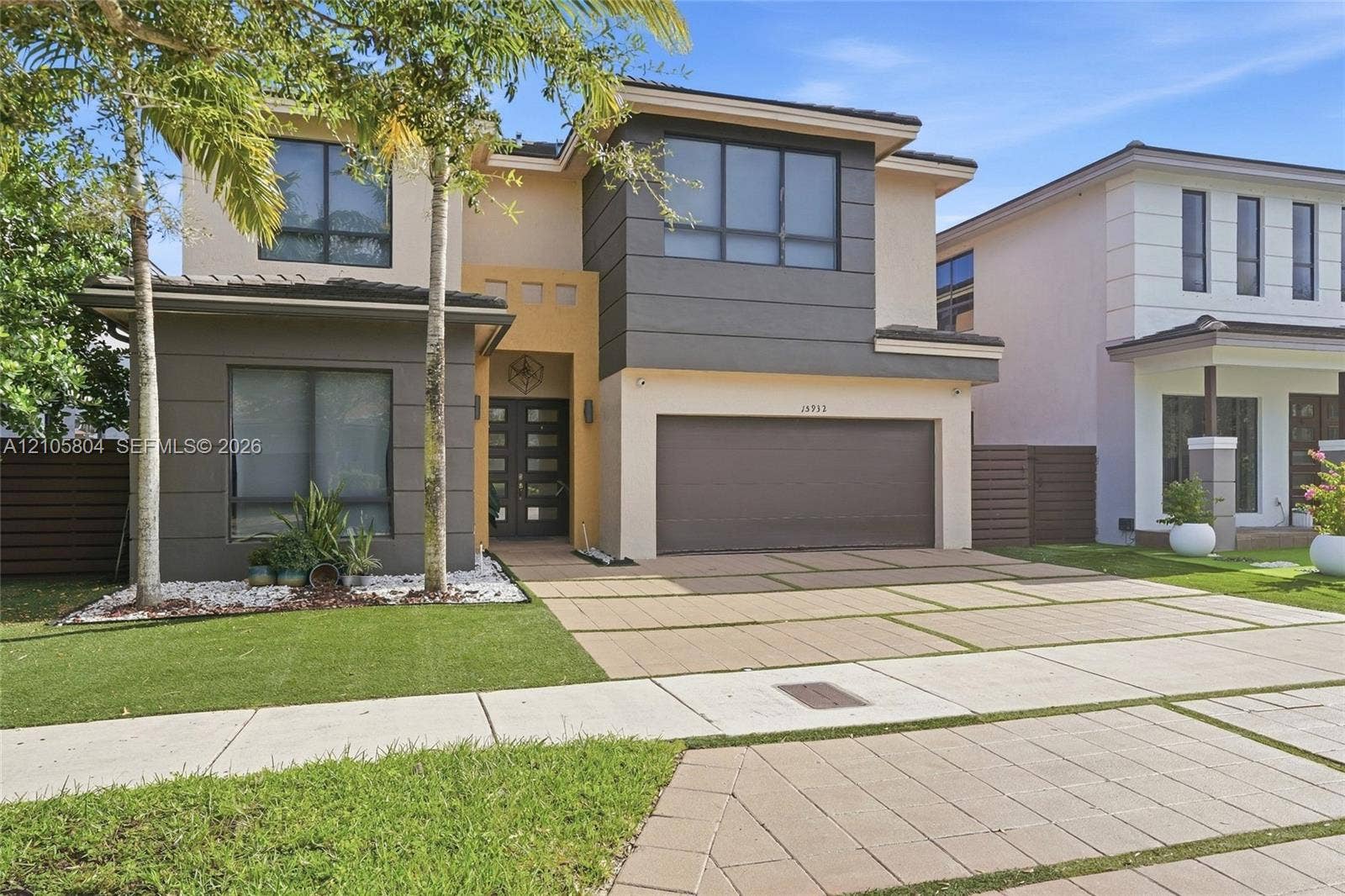 15932 SW 136th Way, Miami, FL 33196 Contemporary exterior featuring two-tone stucco siding, a multi-pane glass entry door, expansive windows, and a paved driveway with integrated turf strips