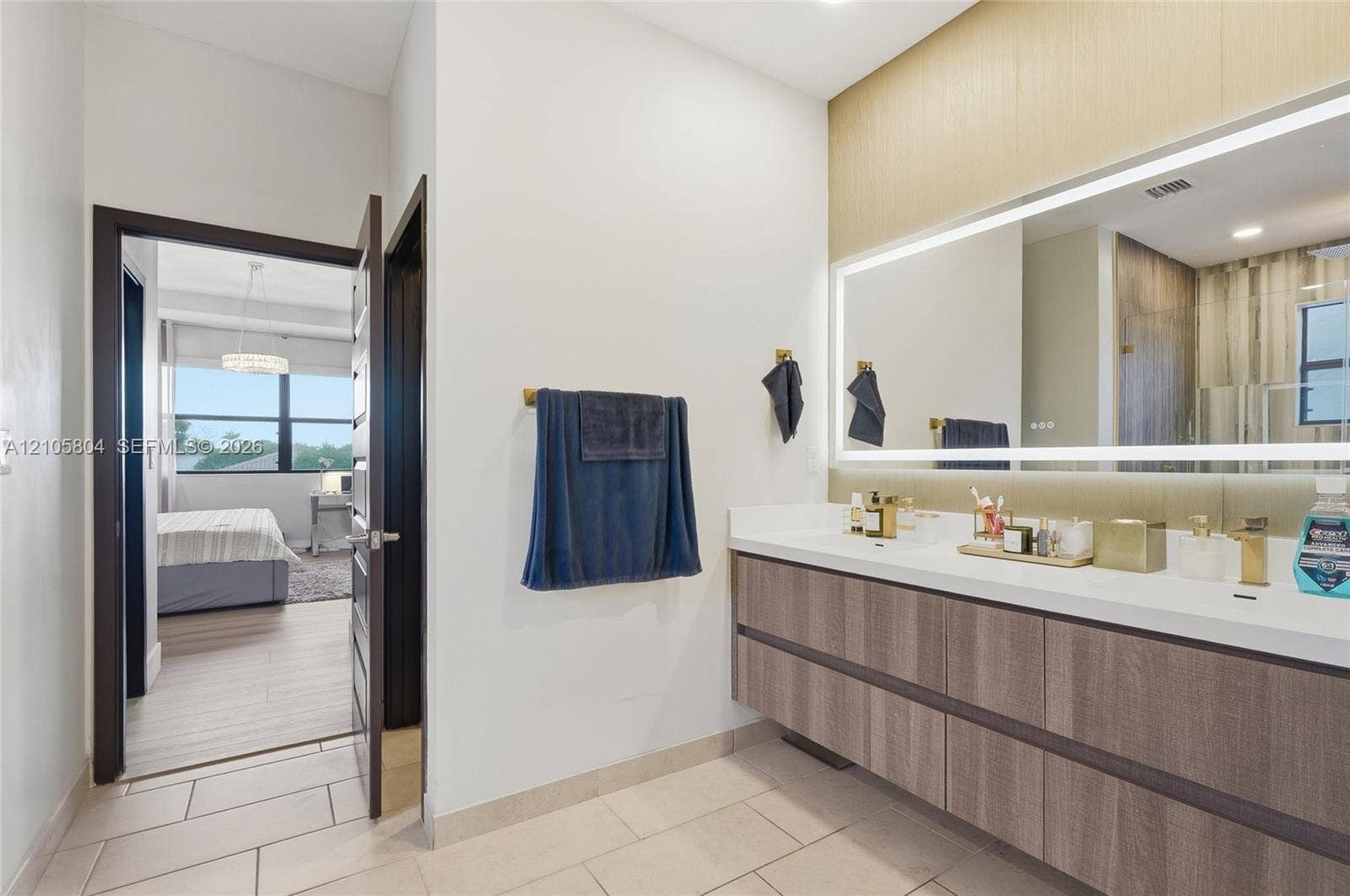 15932 SW 136th Way, Miami, FL 33196 Floating vanity featuring a wood-finish cabinet, integrated double sinks, a large LED-backlit mirror, and gold-tone wall-mounted hardware