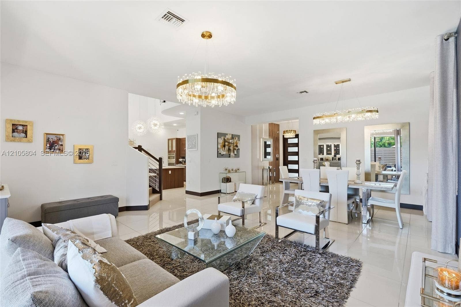 15932 SW 136th Way, Miami, FL 33196 Open-concept living space featuring high-gloss tile flooring, dual tiered crystal chandelier fixtures, and a glass-paneled staircase railing