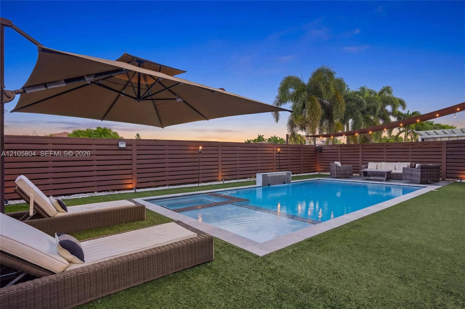 15932 SW 136th Way, Miami, FL 33196 Private backyard featuring an inground swimming pool with an integrated spa, horizontal slat privacy fencing, a stone-finish water feature, and artificial turf