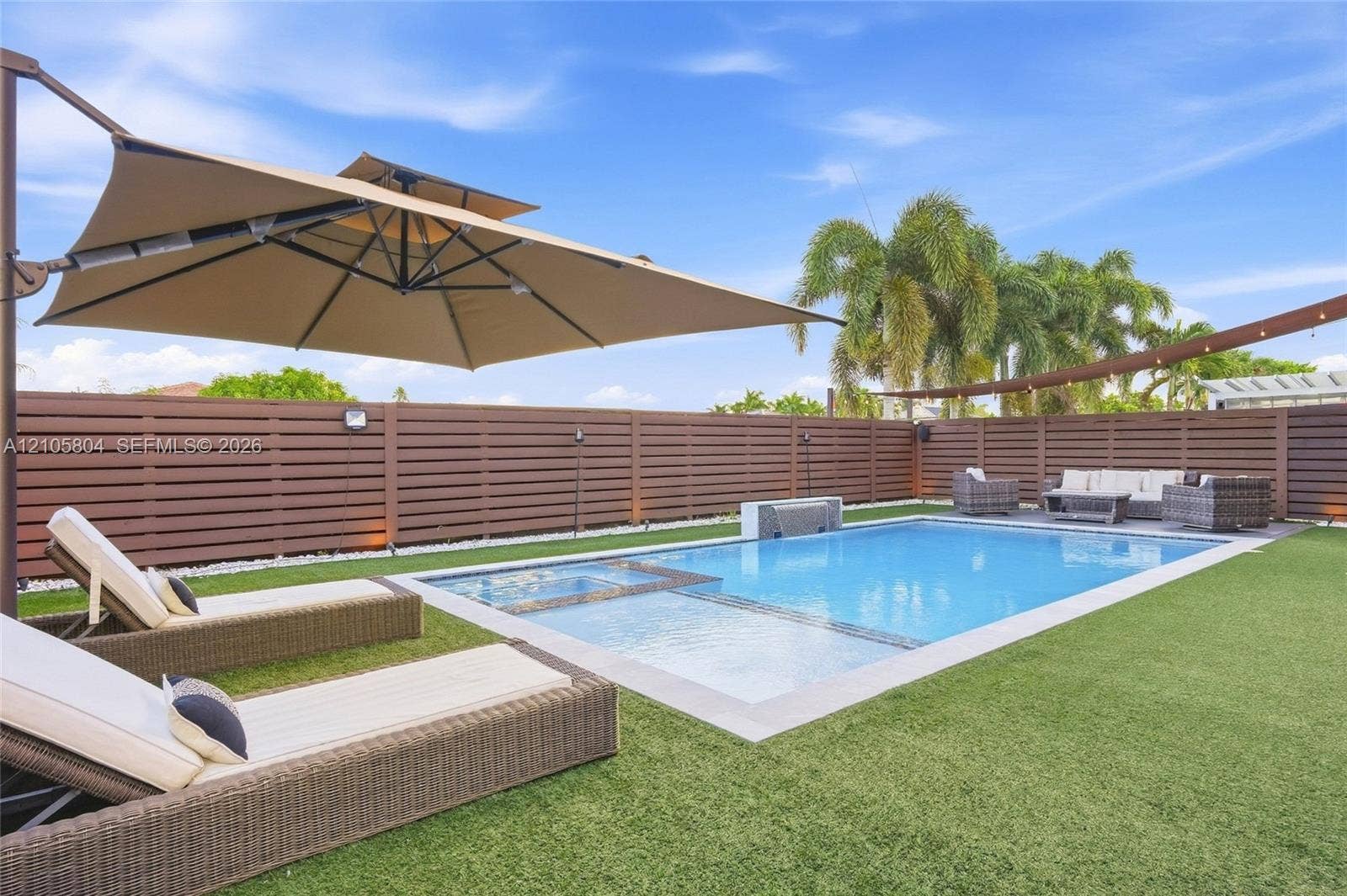 15932 SW 136th Way, Miami, FL 33196 Backyard featuring a rectangular swimming pool with an integrated spa, horizontal slat privacy fencing, artificial turf, and a water feature