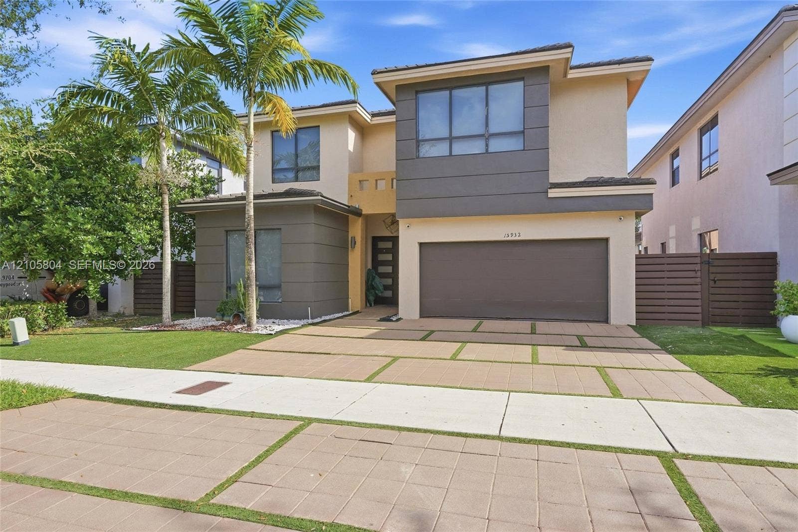 15932 SW 136th Way, Miami, FL 33196 Contemporary two-story exterior featuring a multi-tone facade, large-format window groupings, two-car garage, and a geometric concrete paver driveway with integrated turf strips