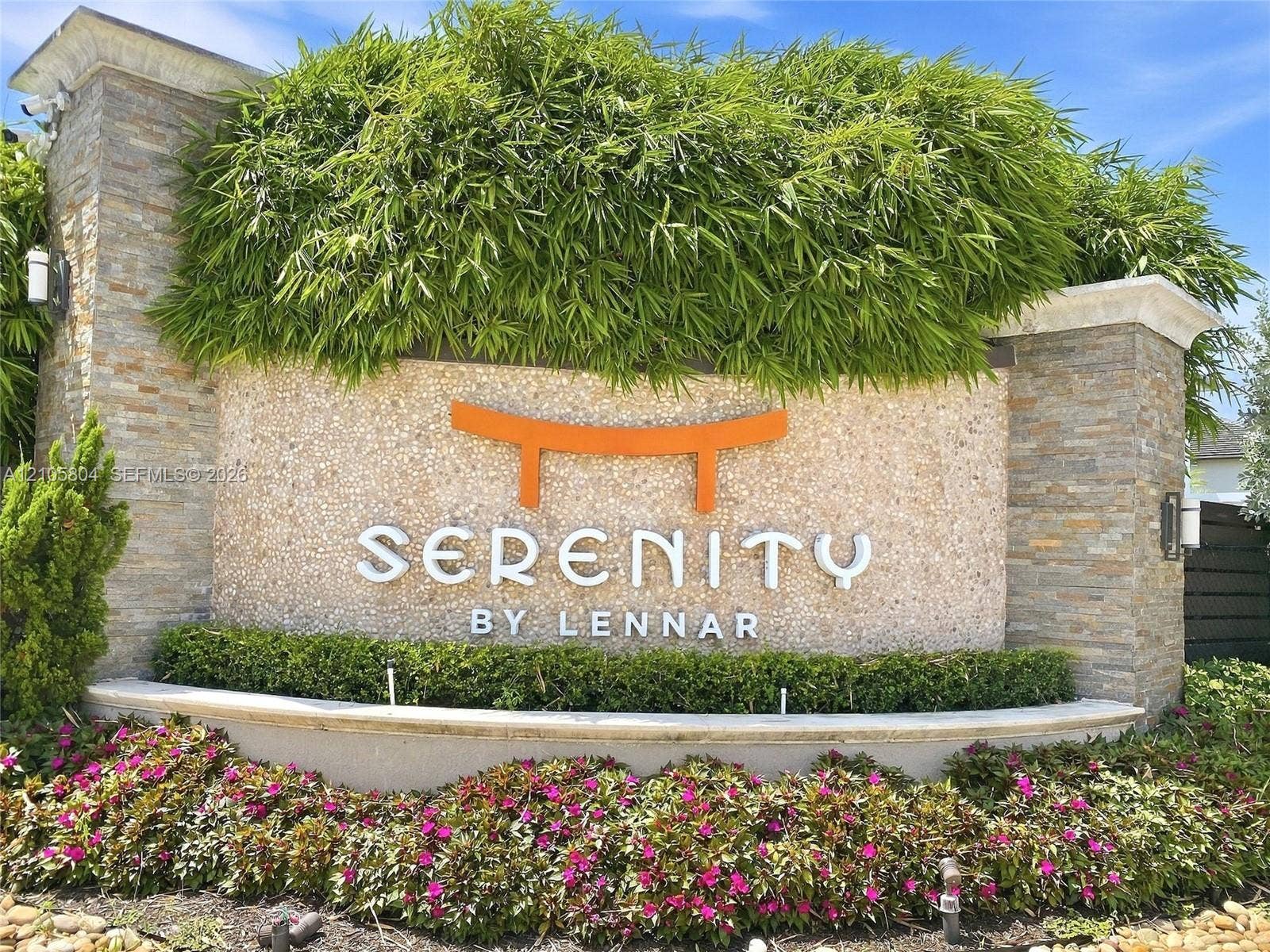 15932 SW 136th Way, Miami, FL 33196 Community entrance sign featuring stacked stone columns, textured masonry, tiered landscaping, and metal accent lighting