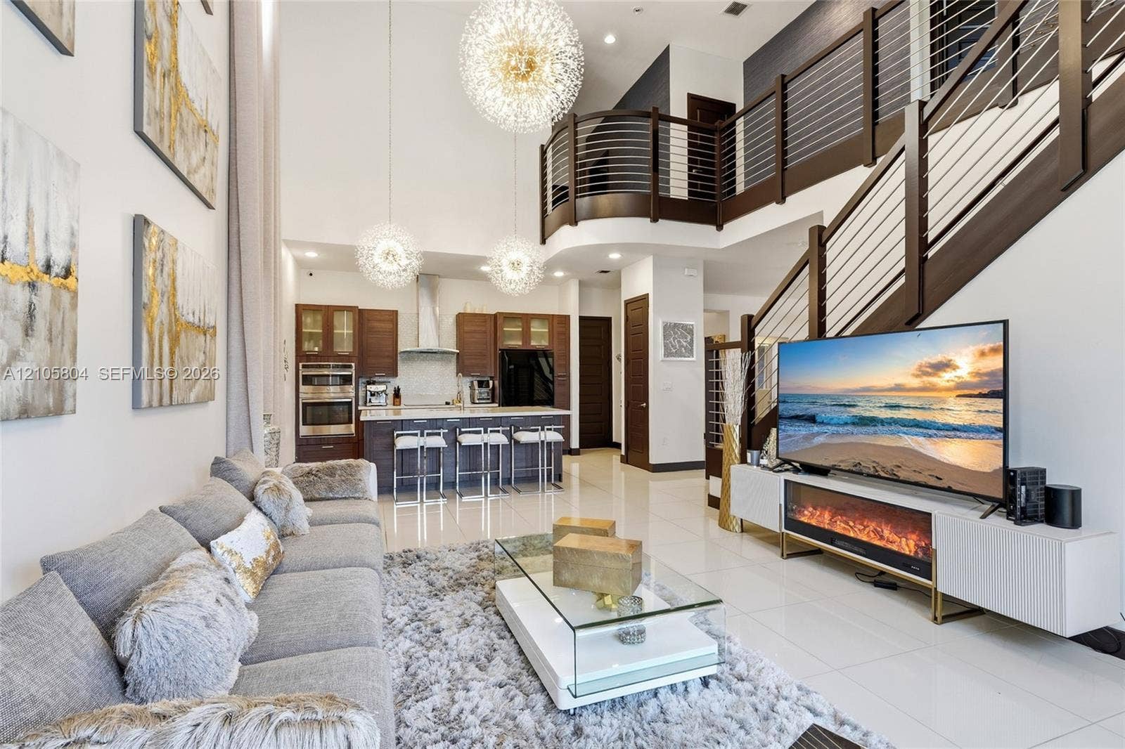 15932 SW 136th Way, Miami, FL 33196 Double-height ceilings featuring tiered spherical pendant lighting, polished stone-finish flooring, and a curved staircase with dark-stained wood handrails and horizontal metal balusters
