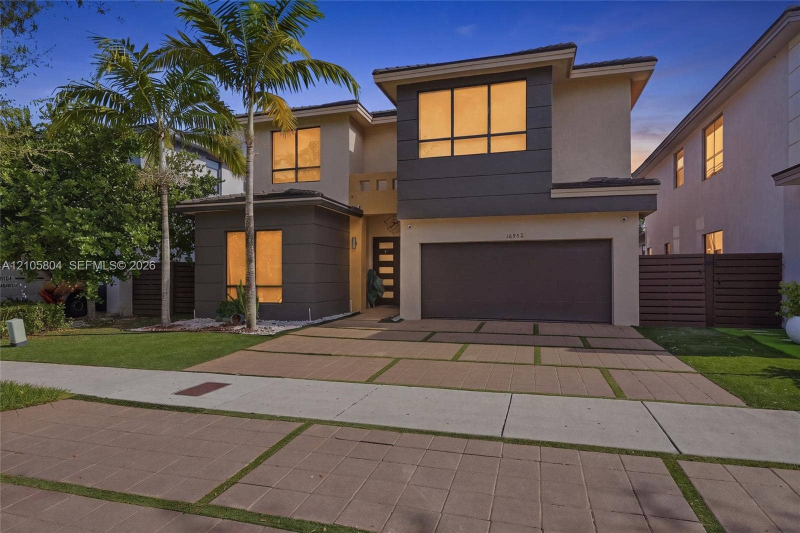 15932 SW 136th Way, Miami, FL 33196 Modern two-story residence featuring a two-tone stucco facade, oversized paver driveway with integrated turf ribbons, multi-pane casement windows, and a multi-panel front door