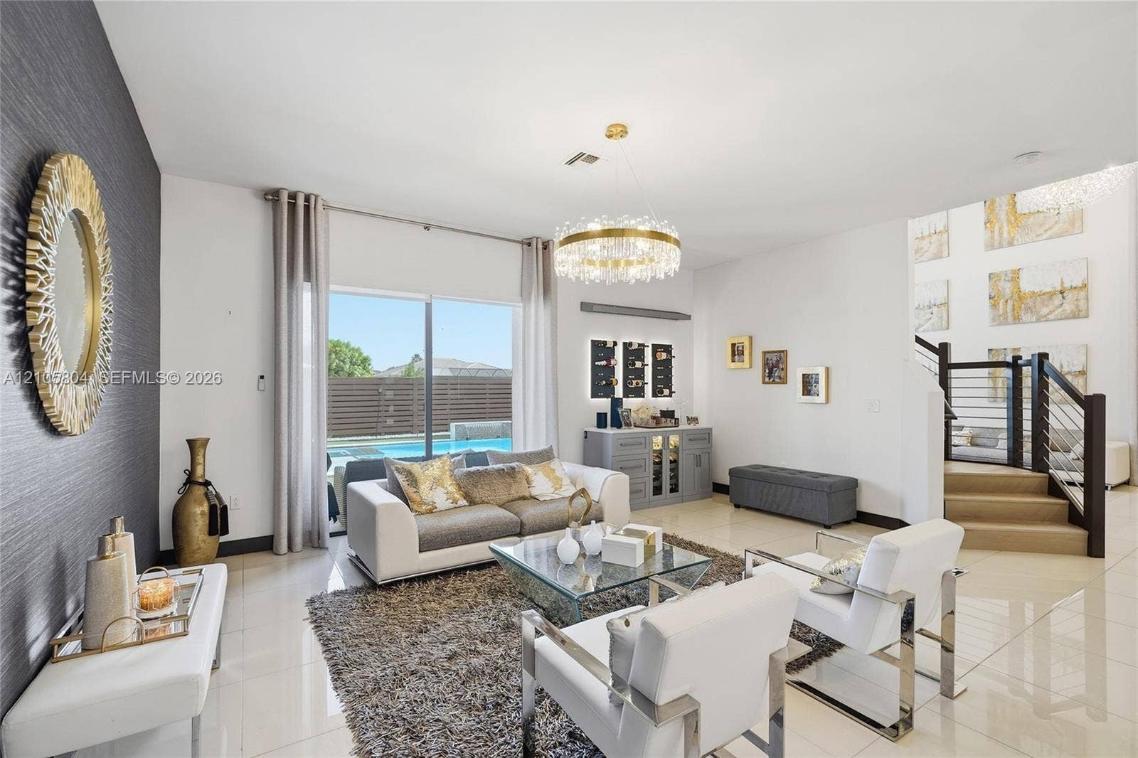 15932 SW 136th Way, Miami, FL 33196 Living area featuring large-format tile flooring, a circular tiered crystal chandelier, a built-in cabinetry unit with integrated lighting, and a staircase with metal horizontal railing