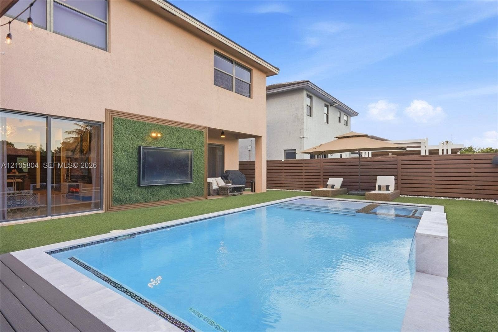 15932 SW 136th Way, Miami, FL 33196 Backyard featuring an in-ground swimming pool with a built-in spa, horizontal wood-slat privacy fencing, artificial turf lawn, and an exterior wall finished with a decorative green panel