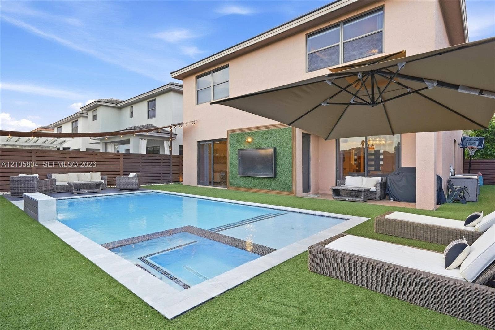 15932 SW 136th Way, Miami, FL 33196 Stucco exterior featuring a pool with an integrated spa, stone-finished coping, artificial turf hardscaping, and a decorative exterior wall panel