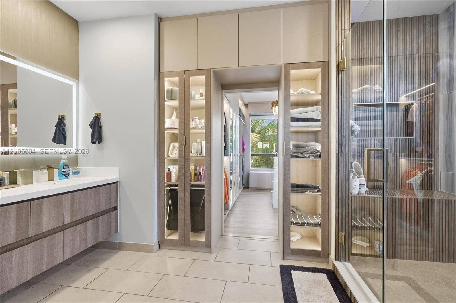 15932 SW 136th Way, Miami, FL 33196 Floating vanity with stone countertop and backlit mirror, floor-to-ceiling built-in cabinetry featuring glass-front display panels, and a walk-in shower with vertical wood-finish wall paneling