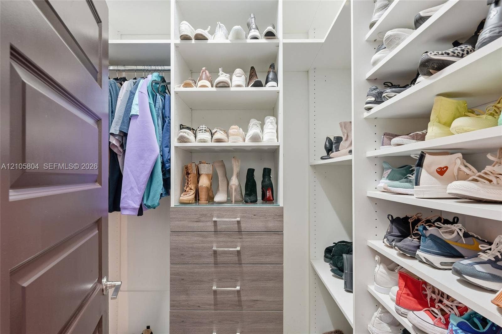 15932 SW 136th Way, Miami, FL 33196 Custom walk-in closet featuring extensive built-in white shelving, integrated wood-finish cabinetry with silver-toned hardware, and a metal clothing rod