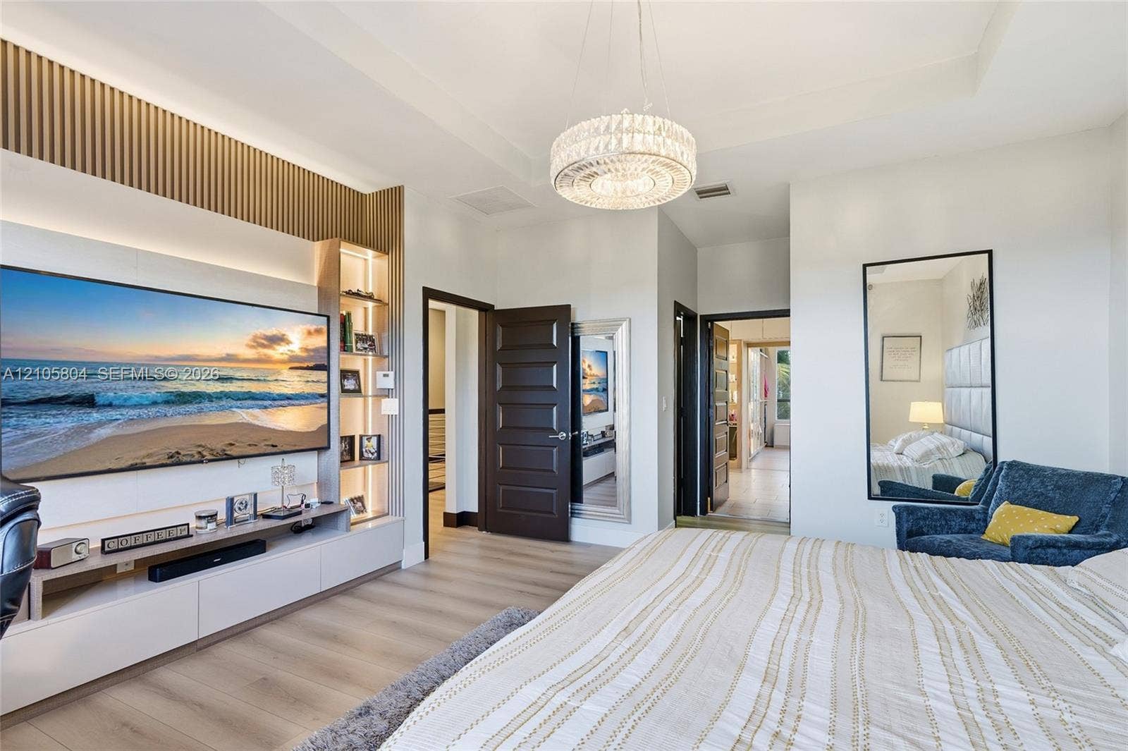 15932 SW 136th Way, Miami, FL 33196 Custom built-in media center with vertical slat wood accent wall, integrated LED display shelving, recessed tray ceiling, contemporary crystal chandelier, and wood-finish flooring